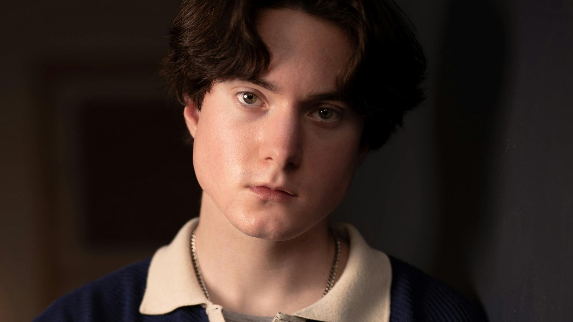 Youthful male posing indoors with soft lighting and a thoughtful expression.