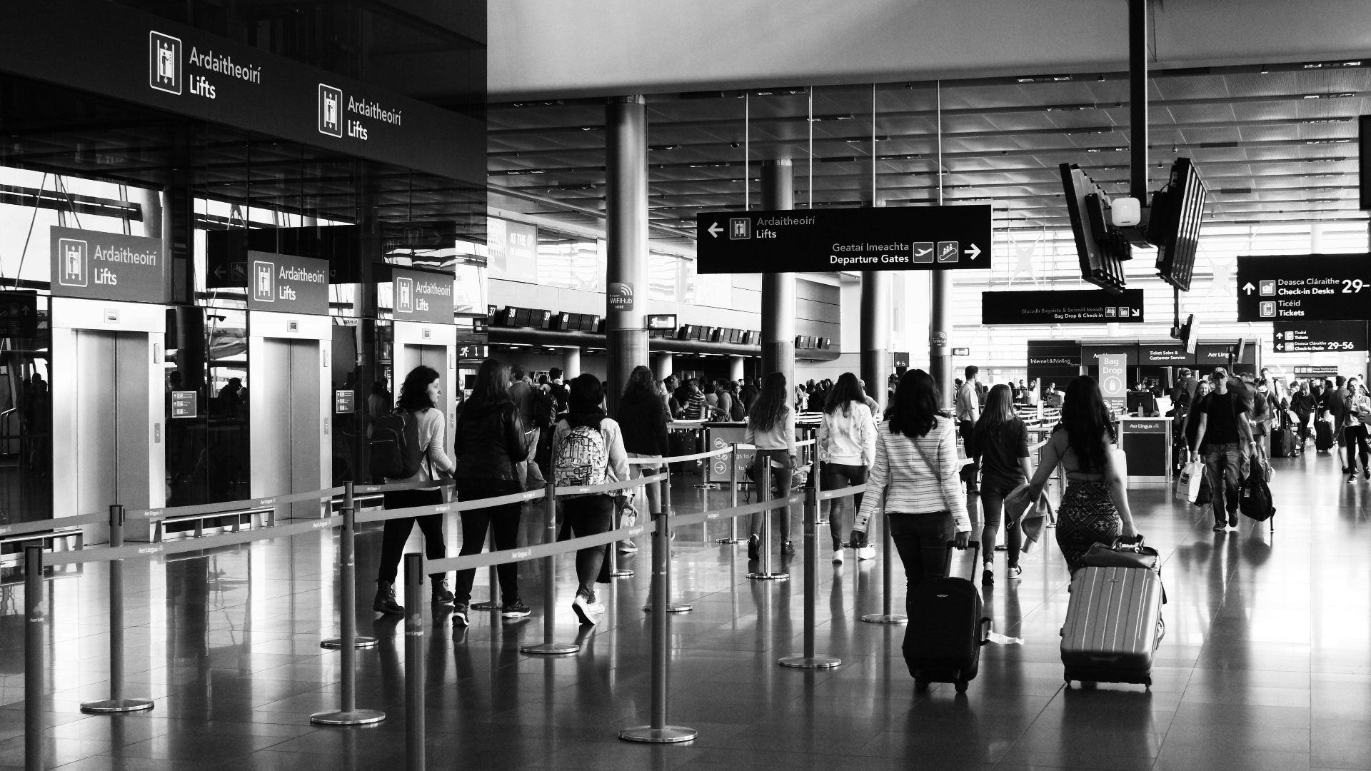 Black and white photo of travelers walking with luggage in a bustling airport terminal.