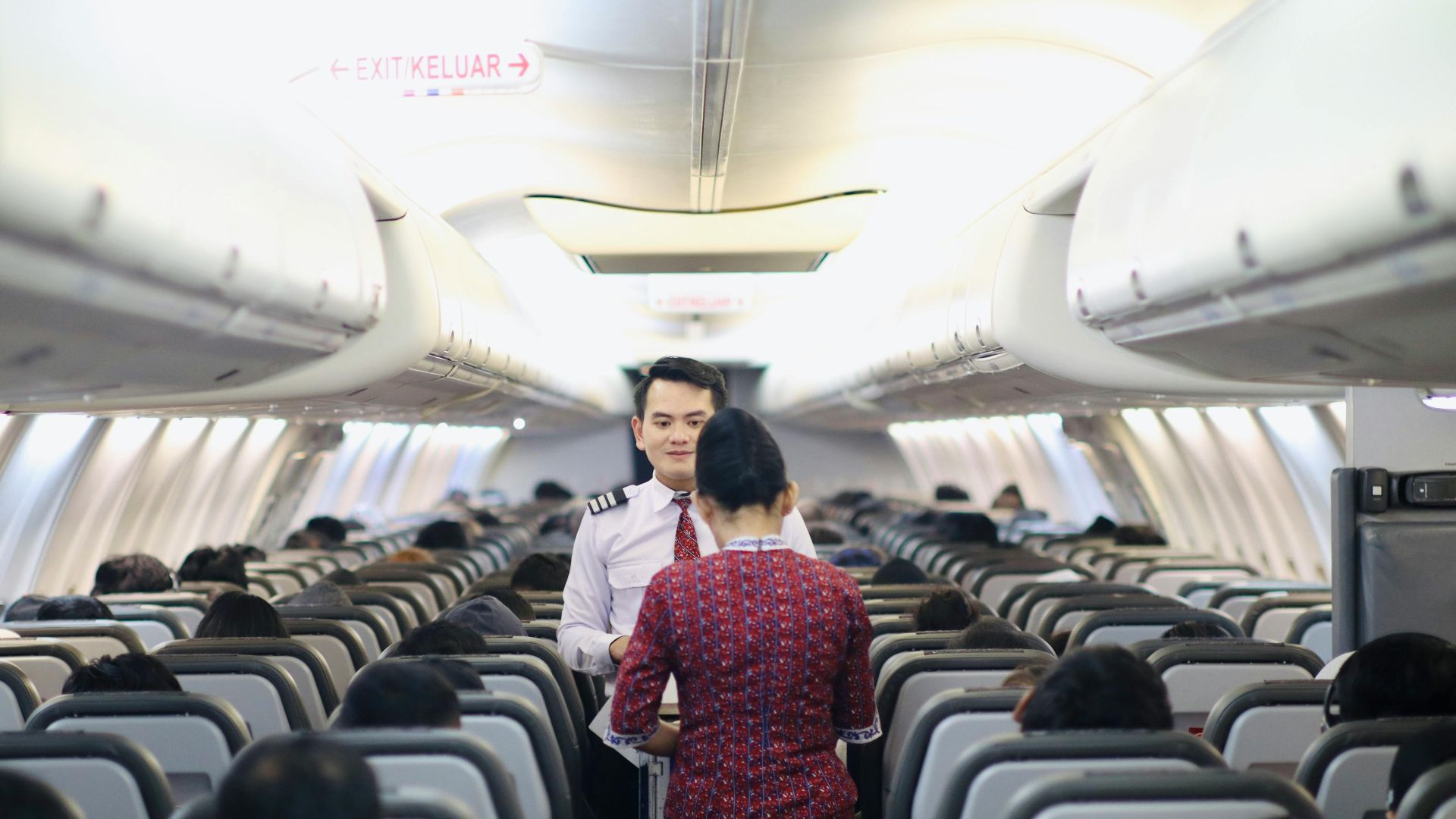 Flight attendants serving passengers inside an airplane cabin during a flight.