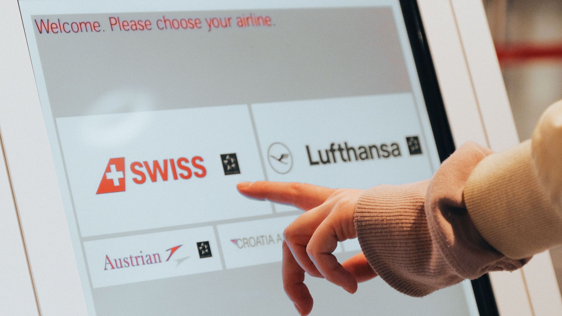 Hand interacting with airport kiosk for airline selection. Modern travel technology.
