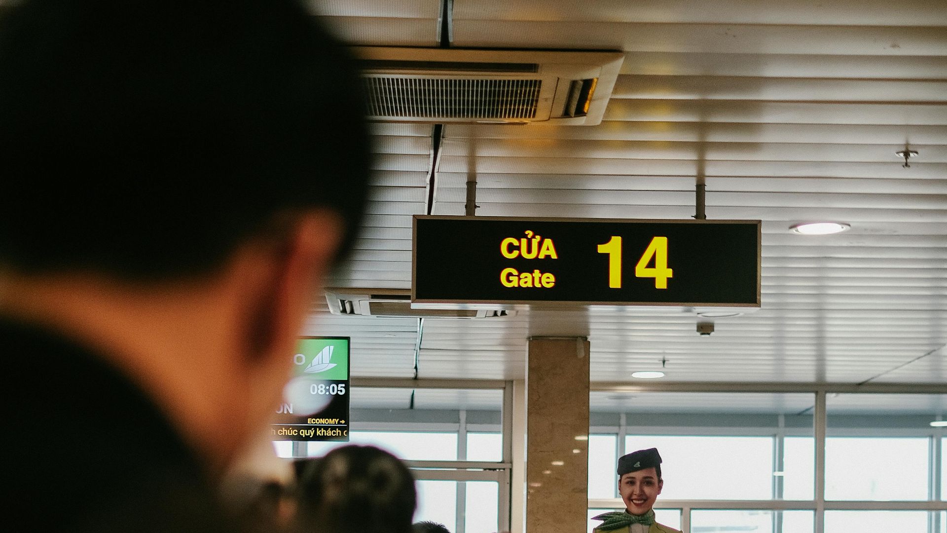 Flight attendant at airport gate 14, Vietnam, offering guidance to passengers indoors.