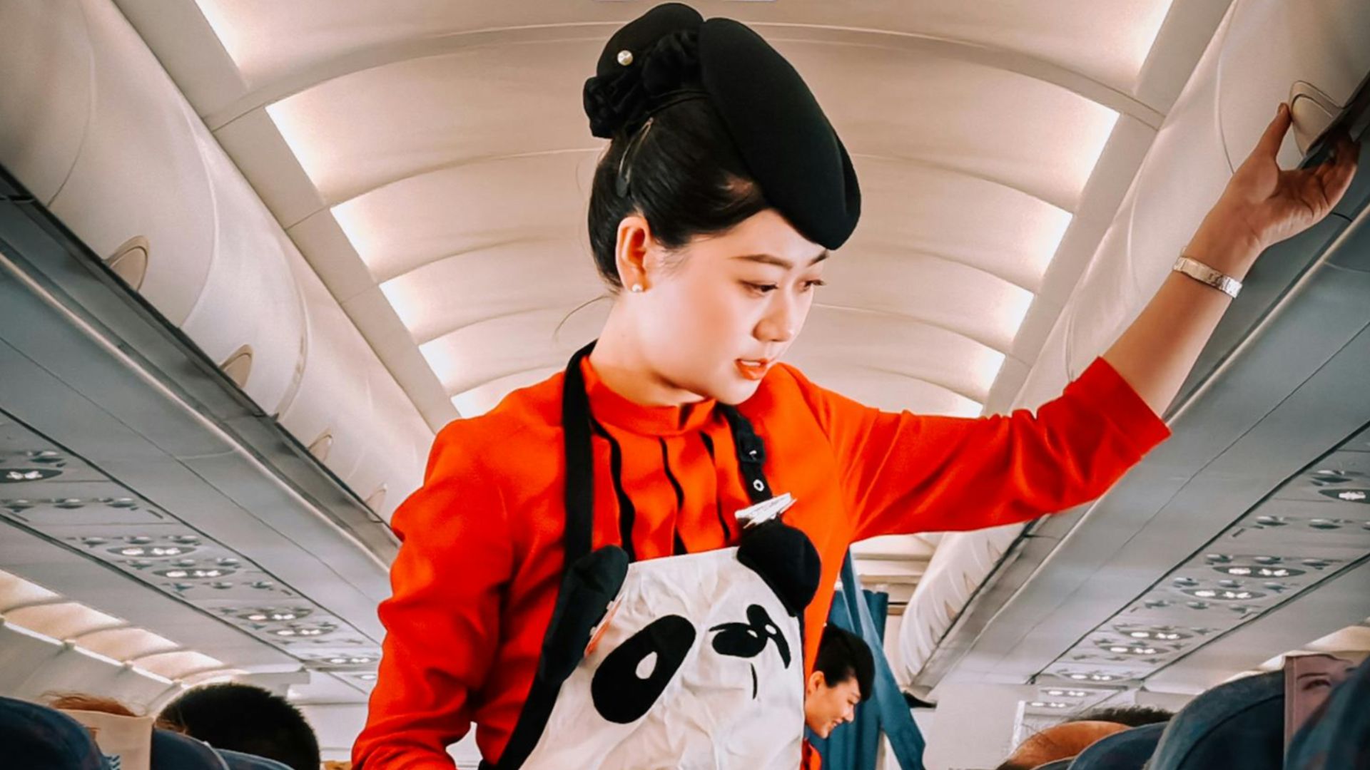Flight attendant in panda-themed apron assisting passengers during flight.