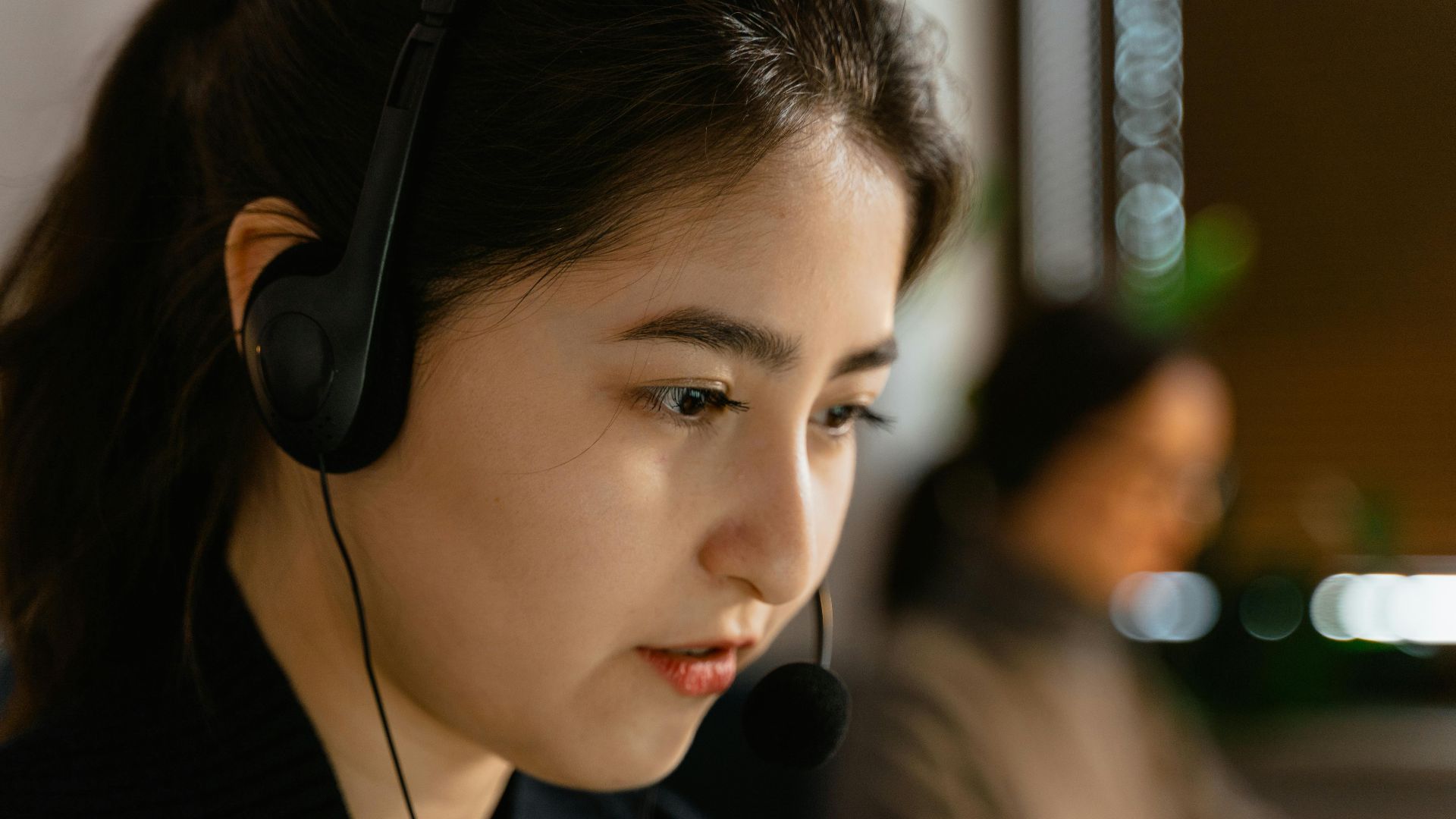 Focused Asian woman in headset providing customer support in office setting.