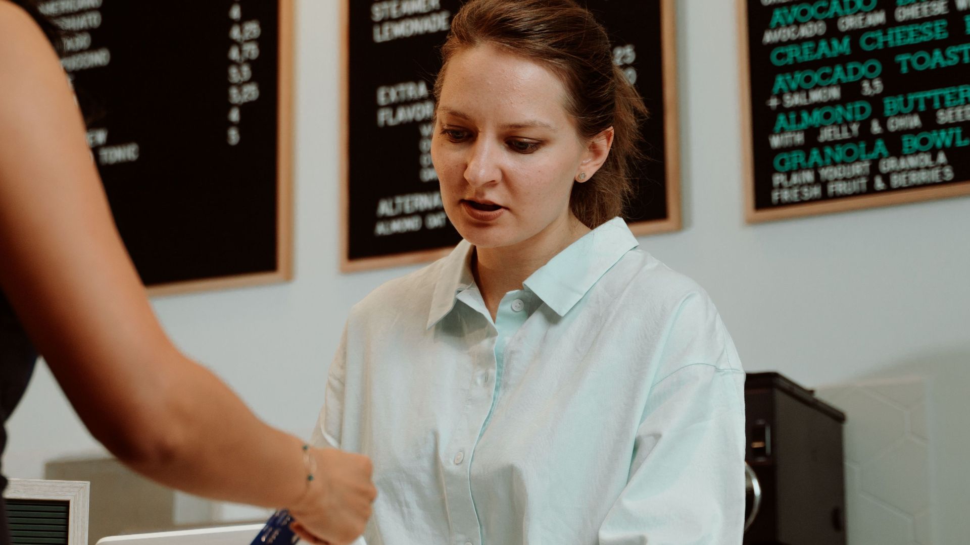 A customer pays with a card at a coffee shop as a barista assists.