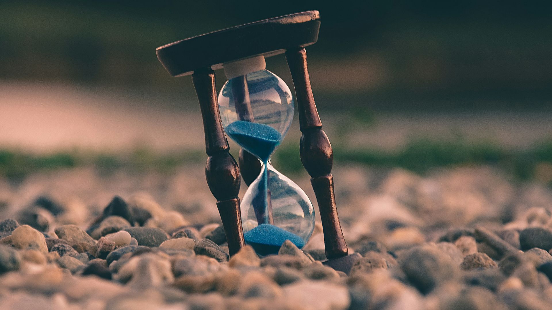 selective focus photo of brown and blue hourglass on stones
