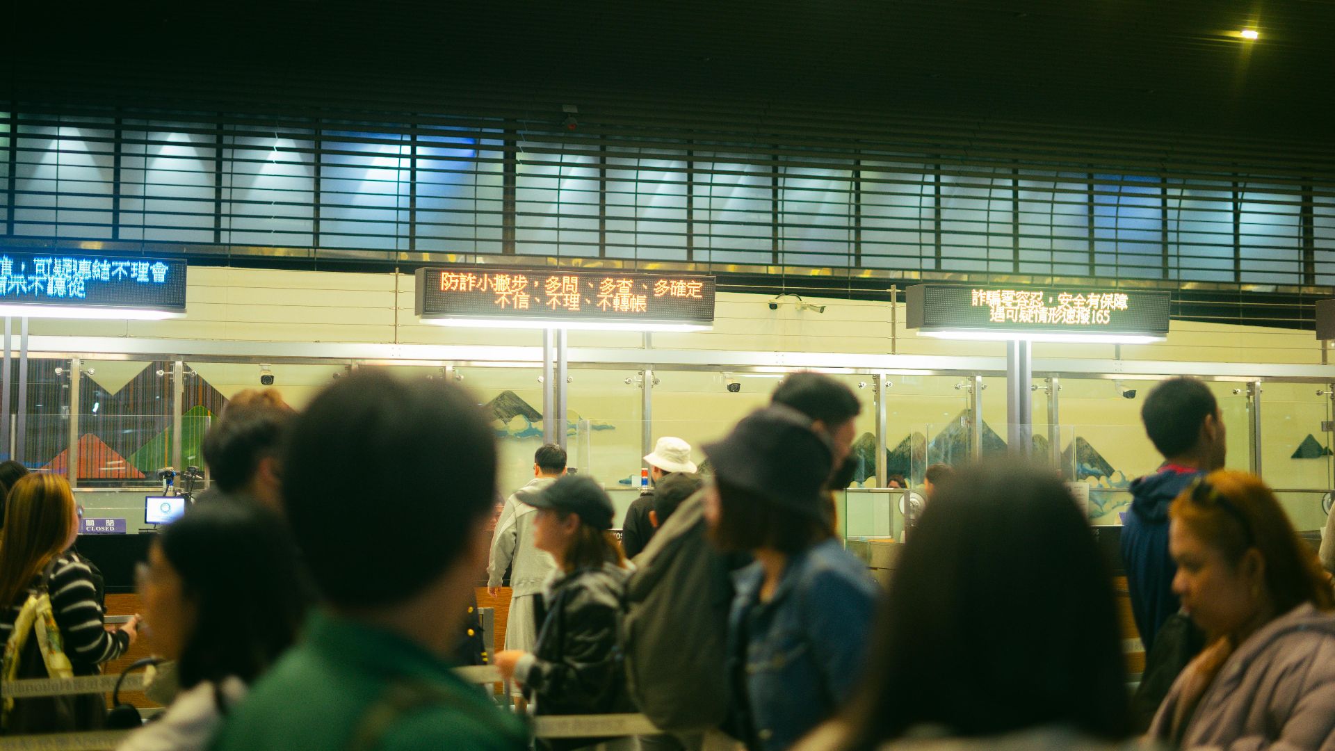 Crowded airport check-in area with people queueing and visible flight information signs.
