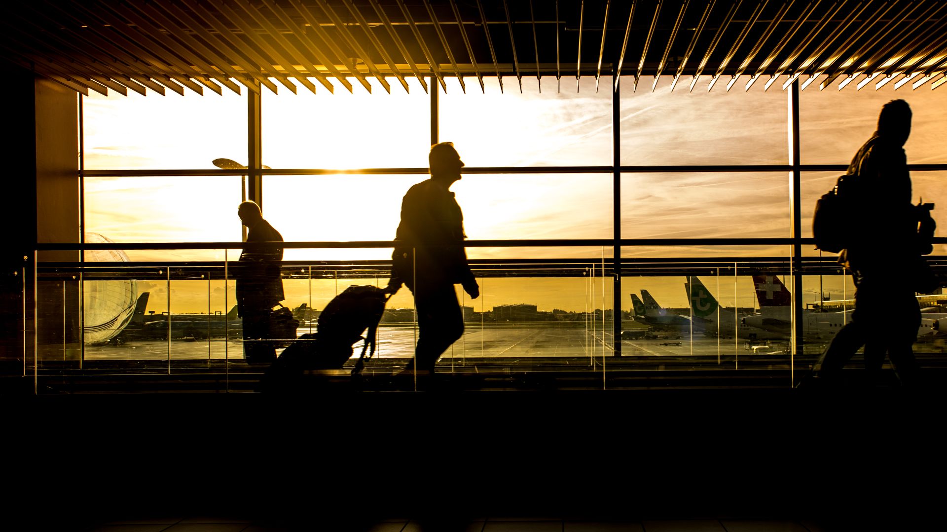 Travelers in silhouette pulling luggage at the airport during a beautiful sunset.