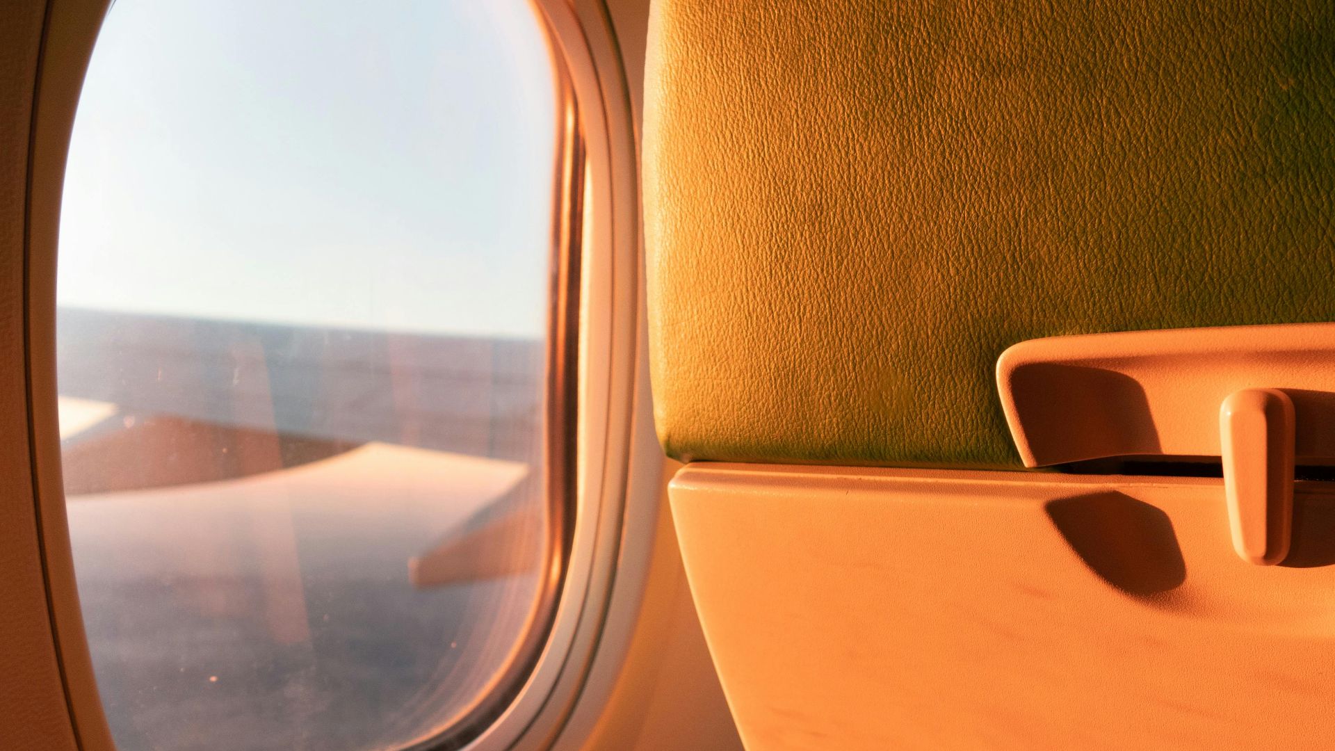 Sunset light illuminating airplane seat and window view during flight.