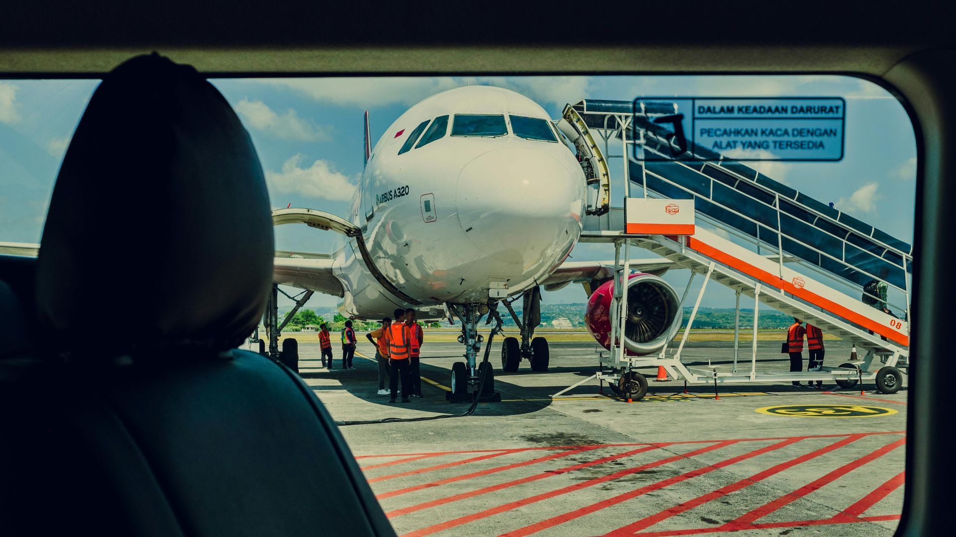 Airplane viewed from a car, parked on the tarmac at an airport with crew working nearby.