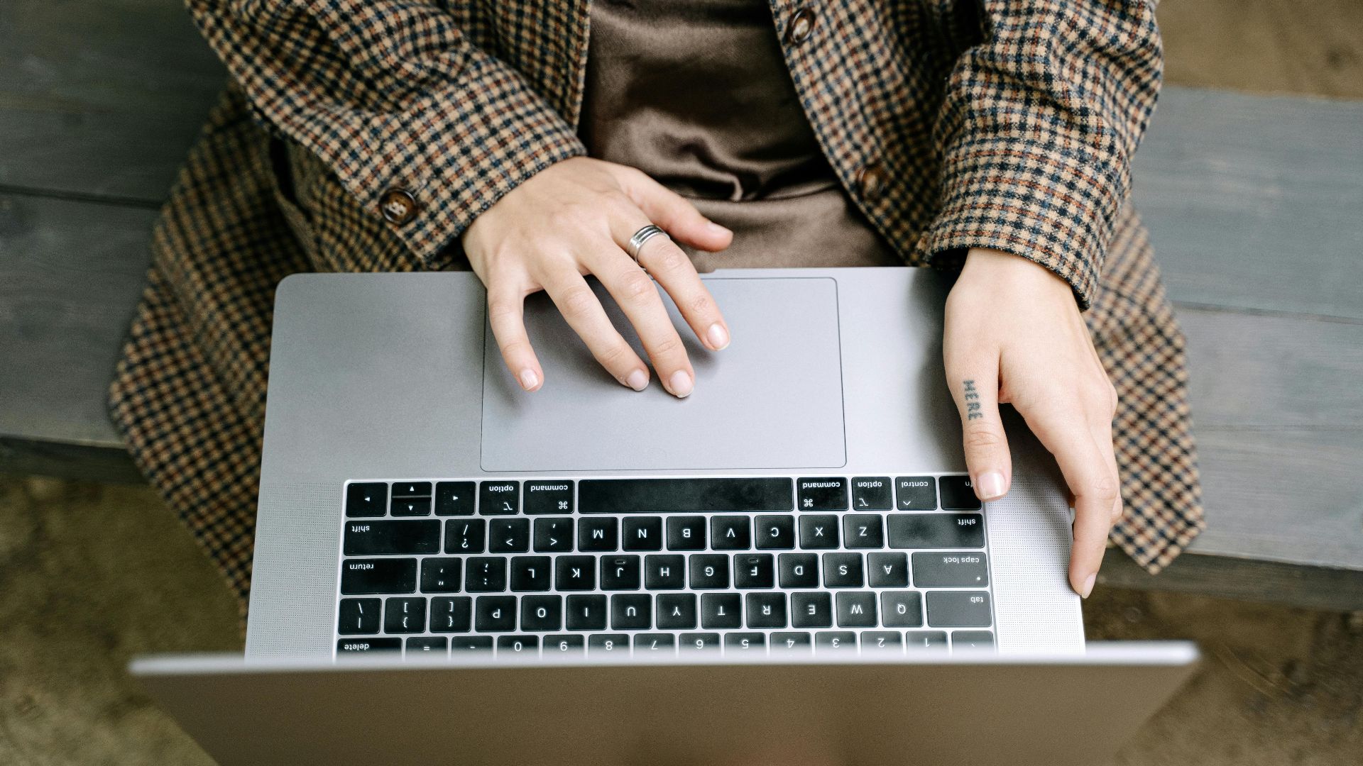 High angle view of individual using a laptop on a wooden bench while wearing a checkered coat.