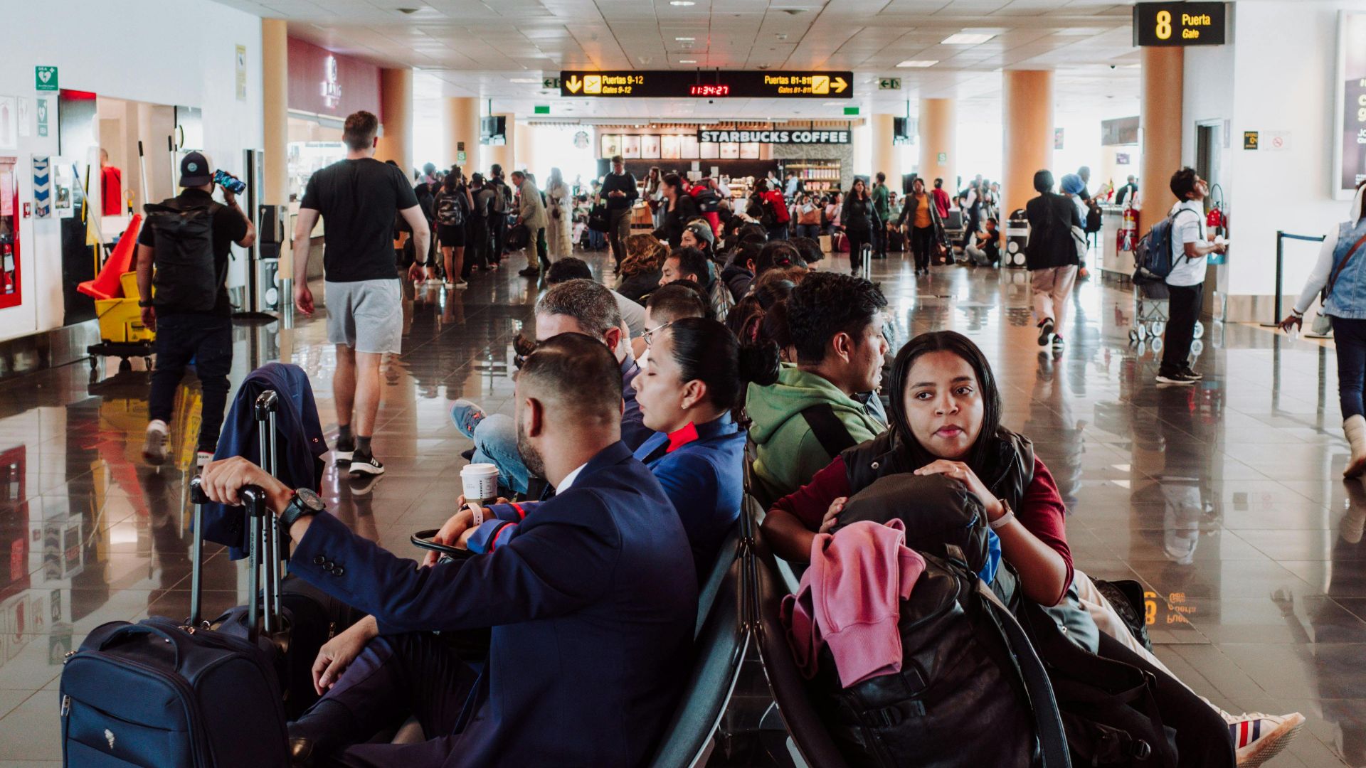 Passengers waiting in a busy airport terminal seating area, with luggage in the modern airport.