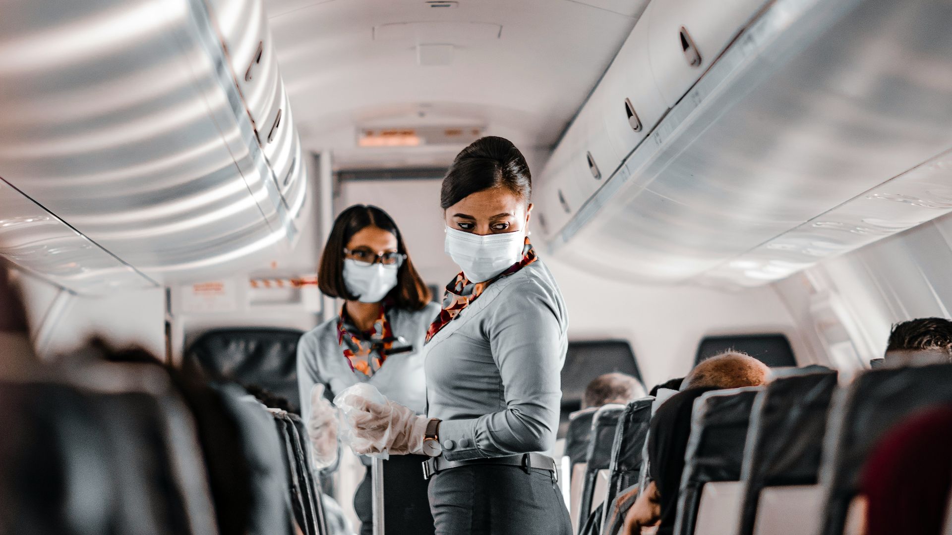 air hostess wearing a facemask standing in the aisle of an aeroplane