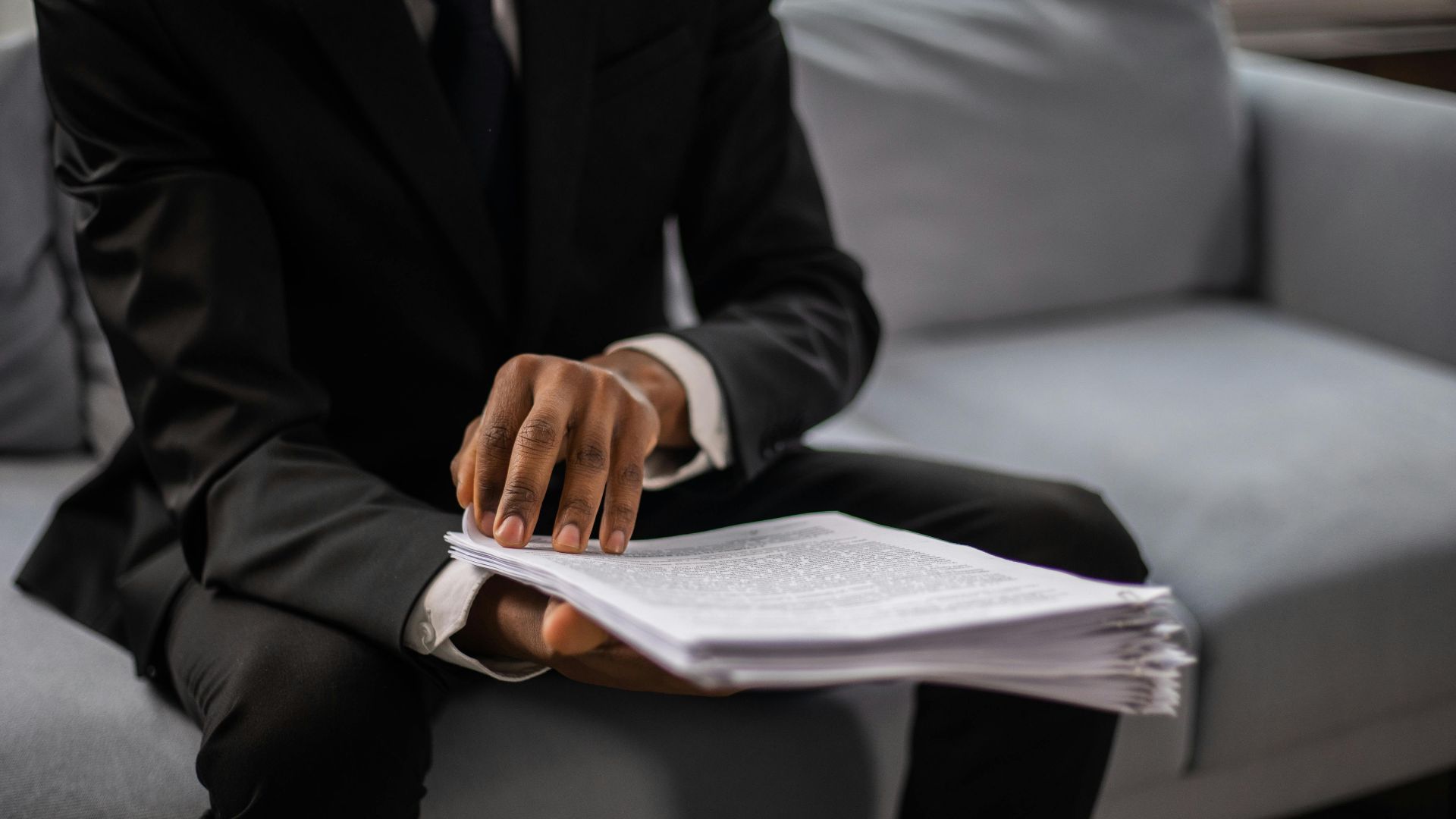 Close-up of a businessman in a suit reviewing documents while seated on a sofa indoors.