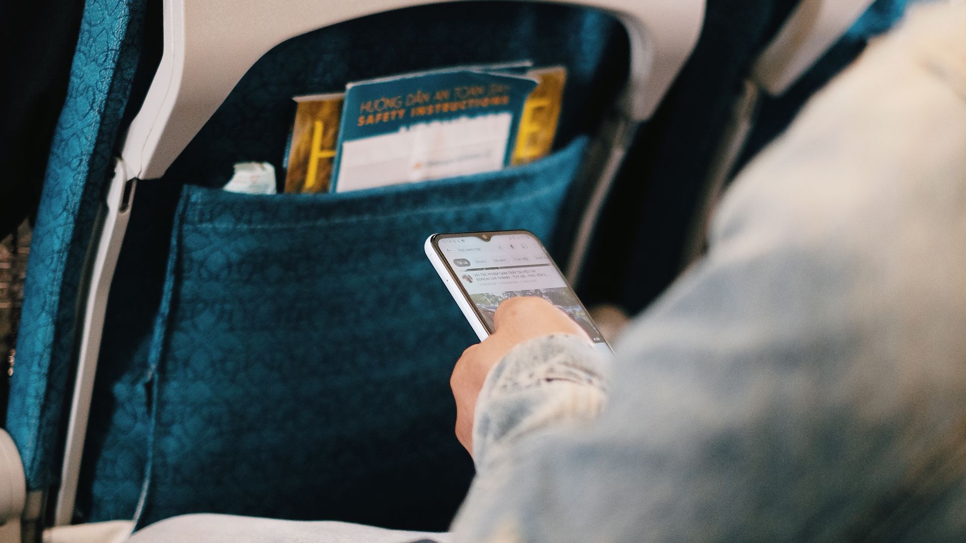 Passenger using smartphone while seated on airplane for entertainment or work.