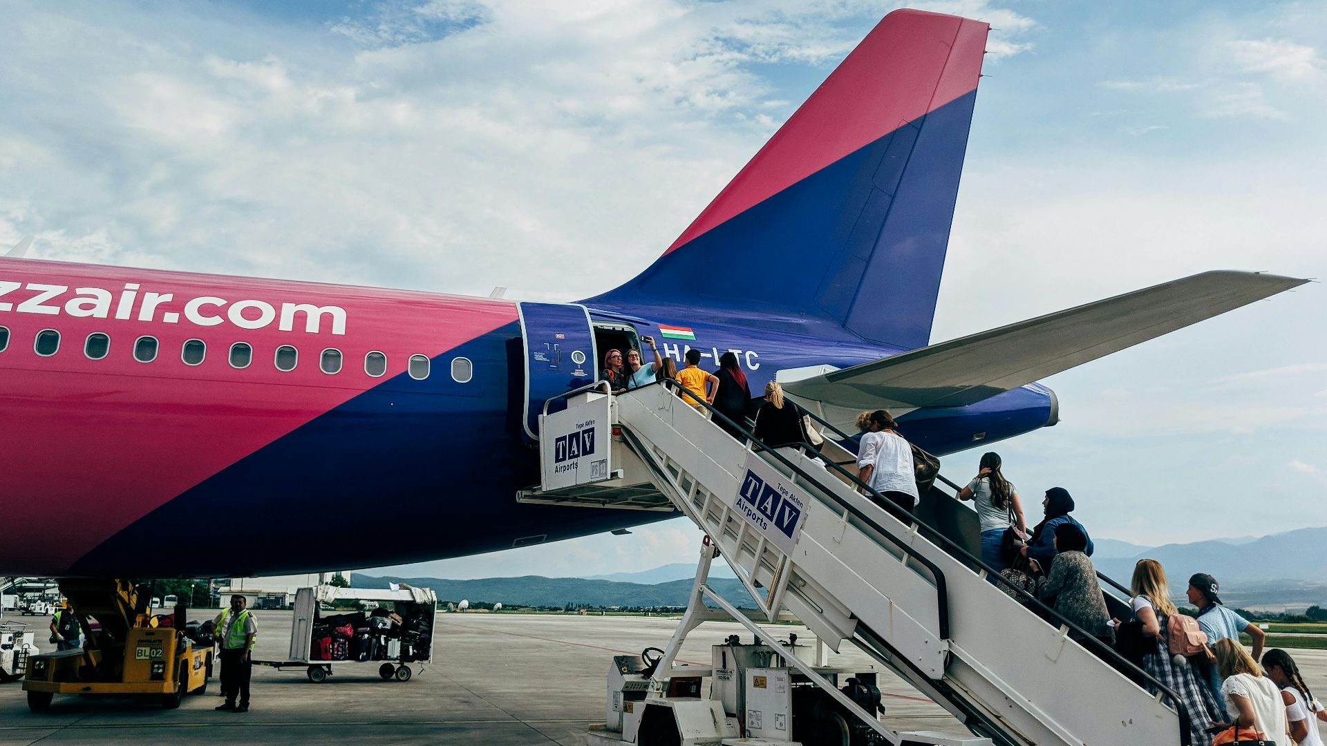 Travelers boarding a WizzAir Airbus A320 jet on a clear day at the airport.