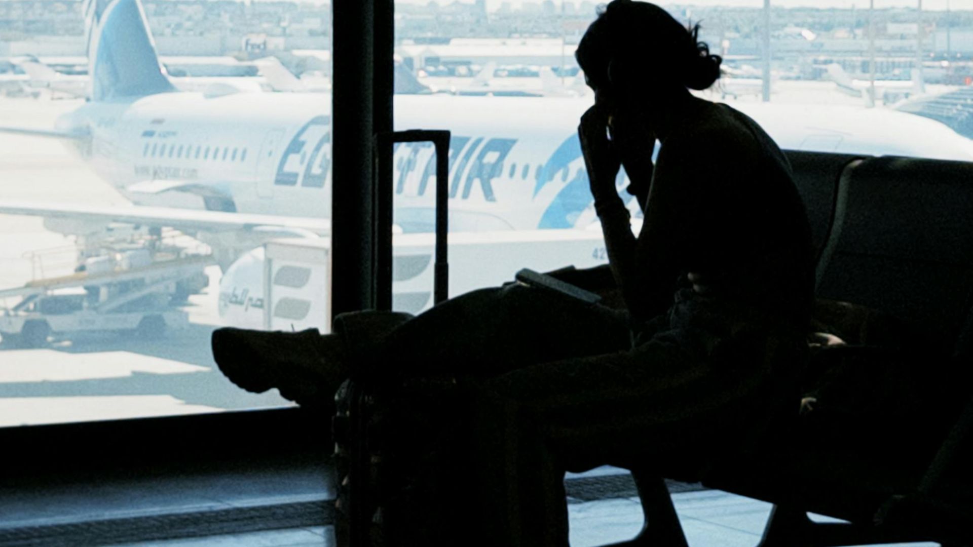 Silhouette of a person at an airport window with airplane view, embodying travel anticipation and solitude.