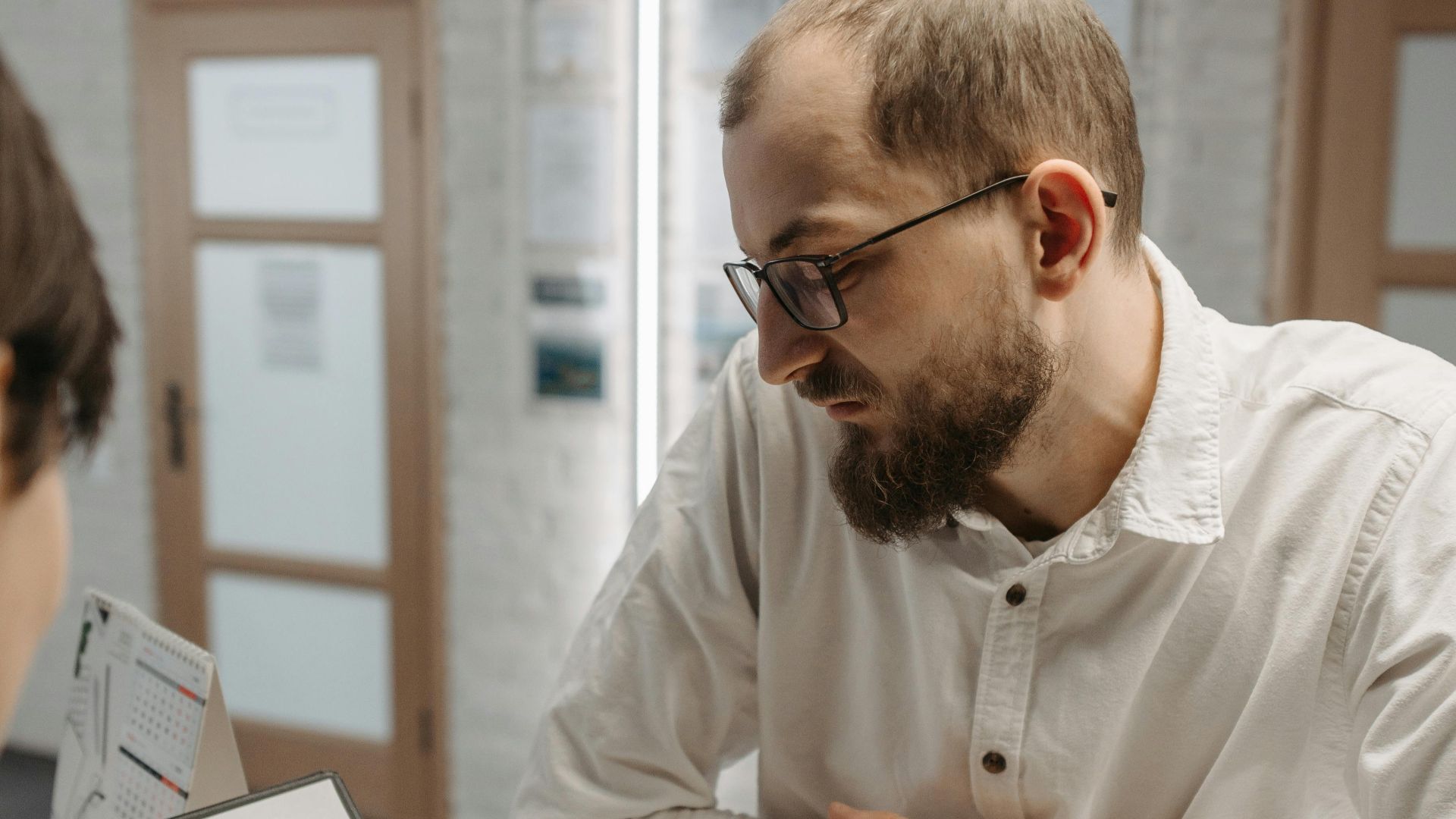 A thoughtful man leaning on a reception counter while discussing plans indoors.