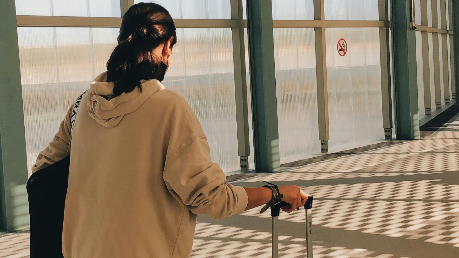 Back view of a woman walking with luggage through an airport terminal.