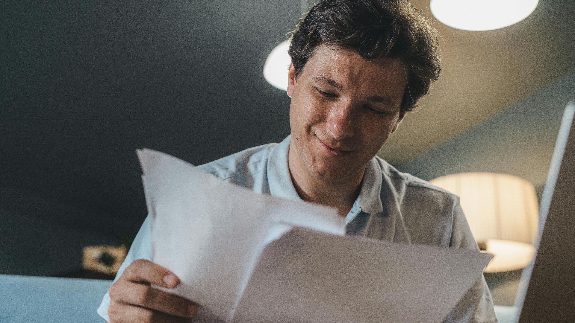 A cheerful man reading papers in a cozy indoor setting, radiating positivity.