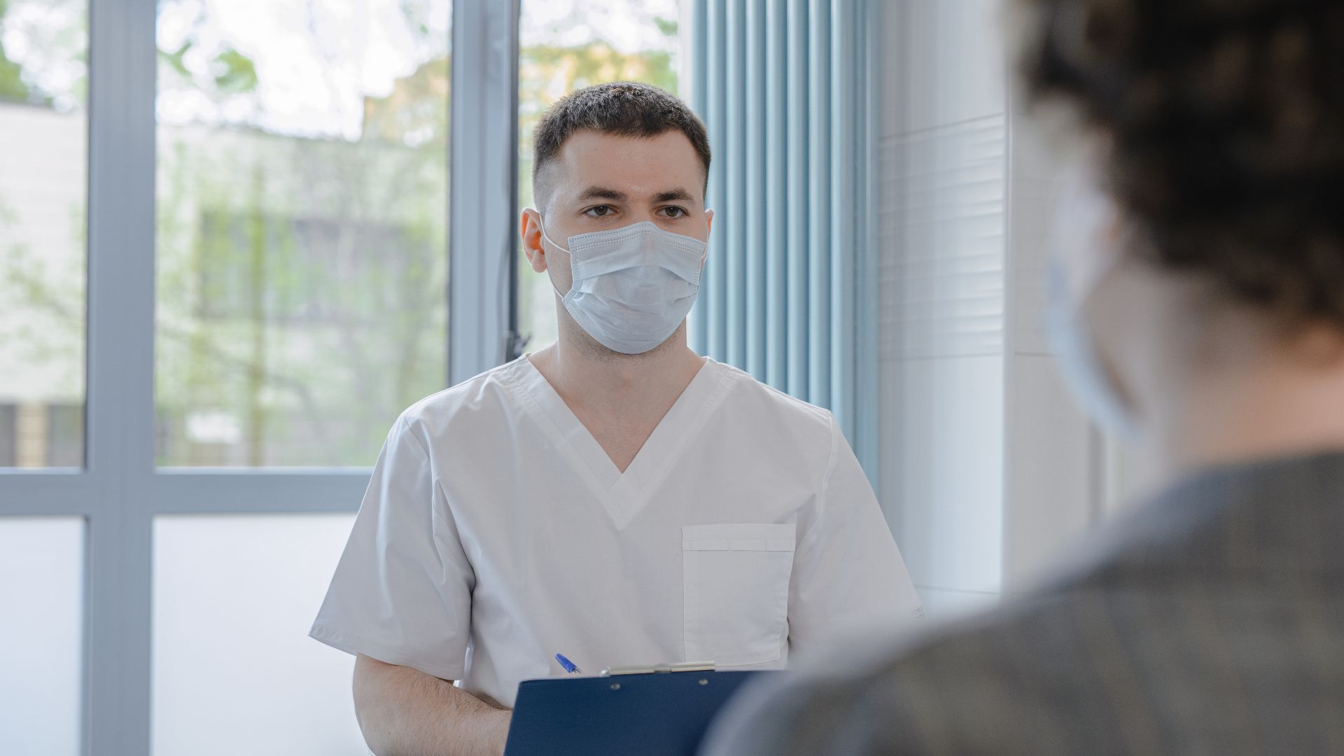 Medical professional in scrubs consulting with a patient while taking notes.