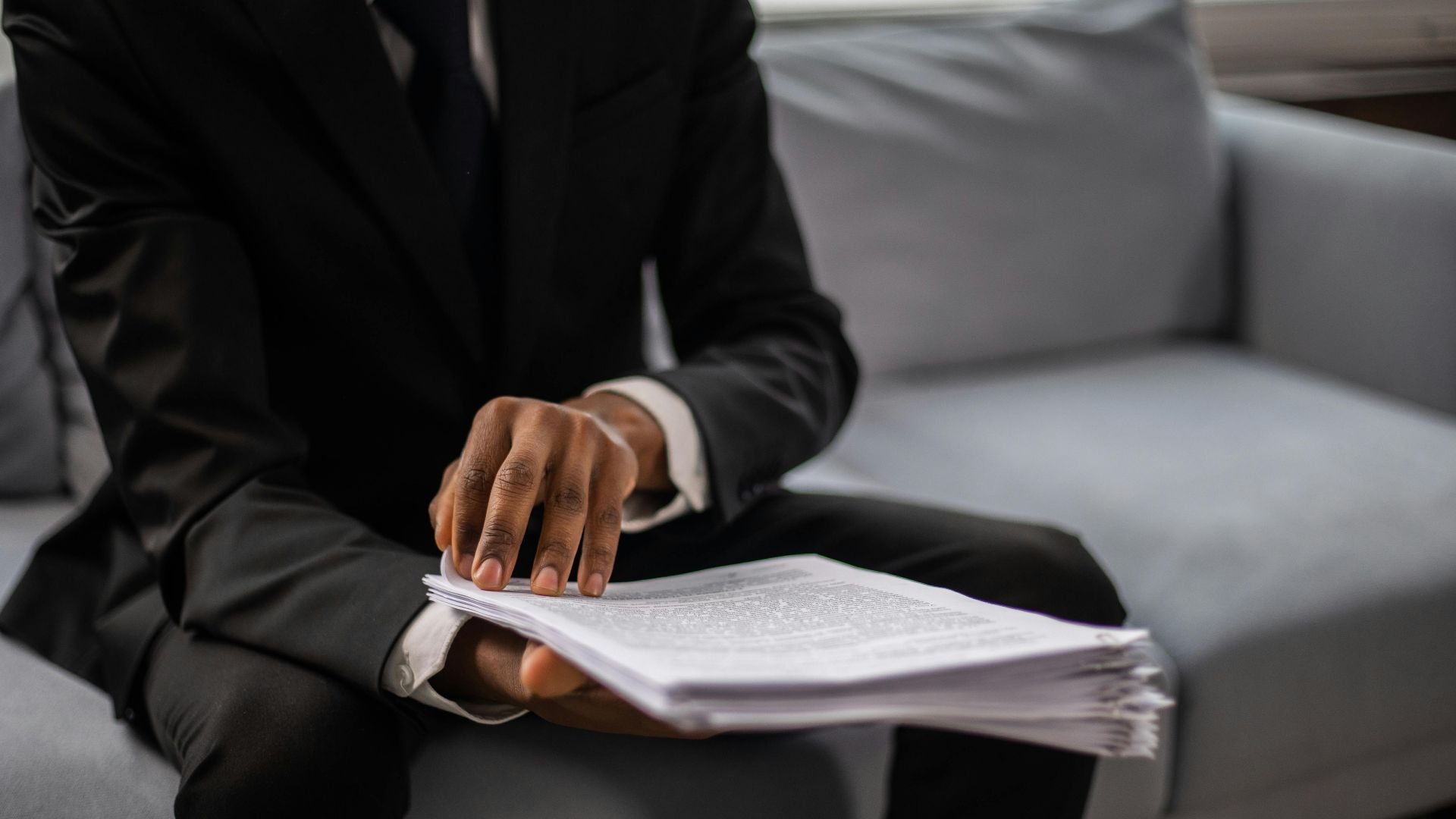 Close-up of a businessman in a suit reviewing documents while seated on a sofa indoors.