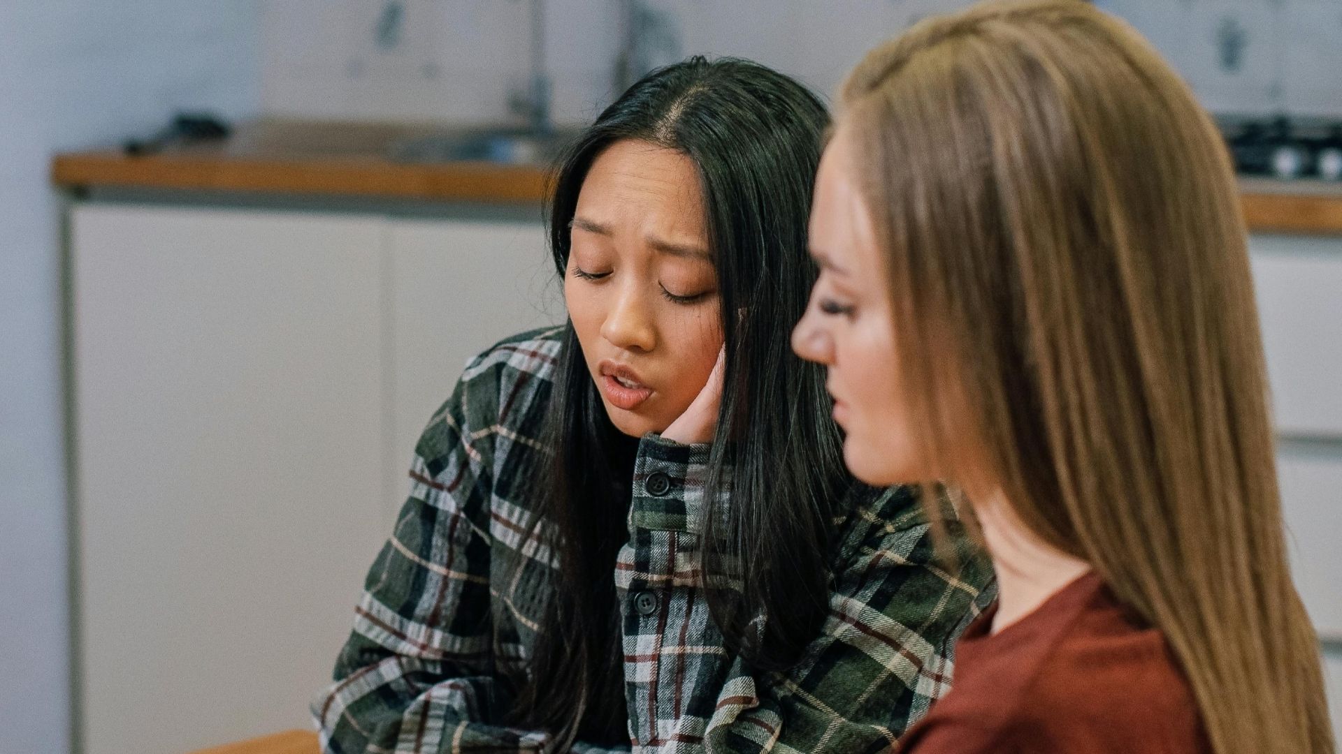 Two women in conversation at a table, offering emotional support over tea in a cozy indoor setting.