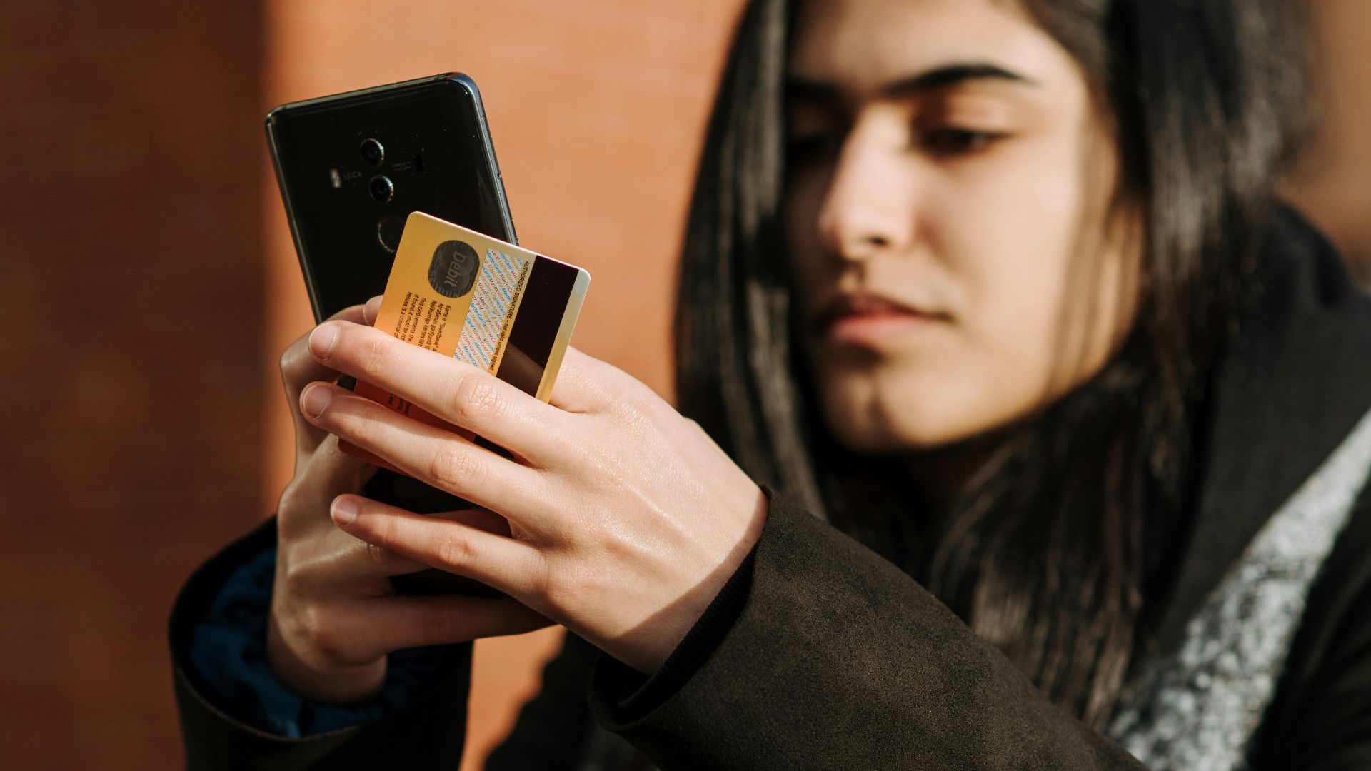 Crop young Hispanic female shopper with debit card making purchase on cellphone near takeaway beverage in cafeteria