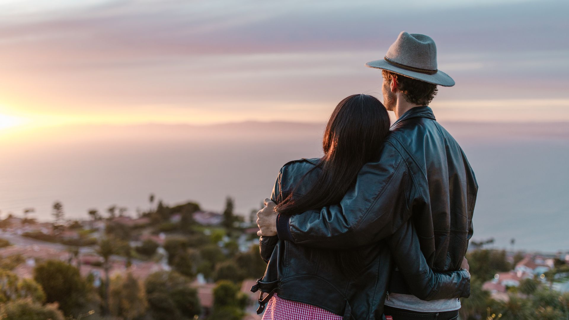 Romantic couple embraces while watching the sun set over the ocean, creating a tranquil moment.