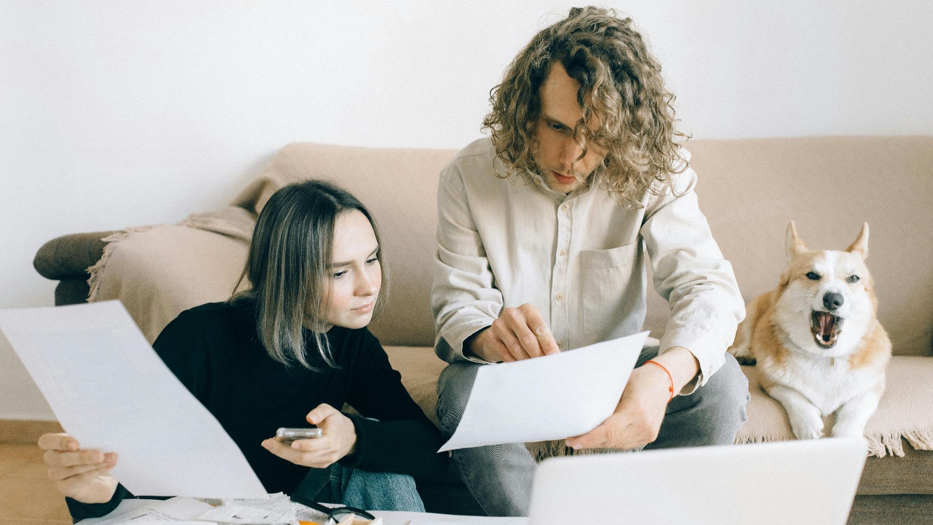 A couple working remotely at home with documents and a dog on the sofa.
