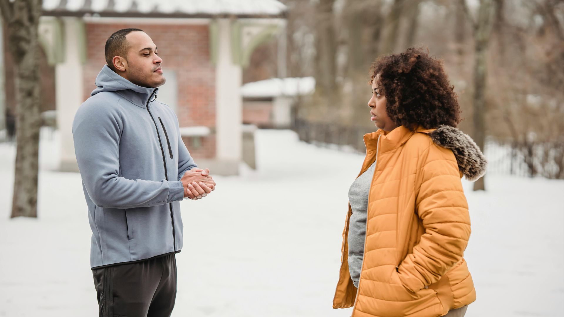 Side view of plump African American and black man in sportswear looking at each other while standing on snowy ground during workout