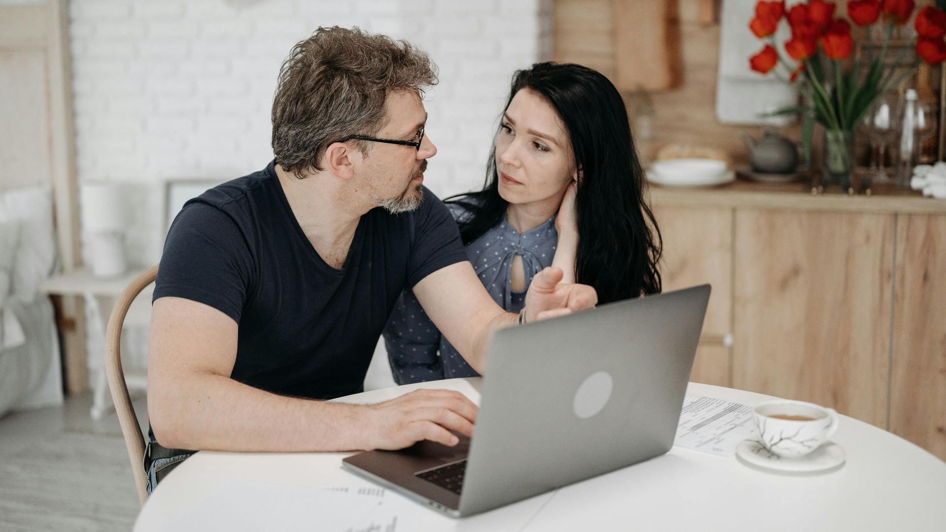 A couple engaged in discussion while using a laptop at a cozy home setting.