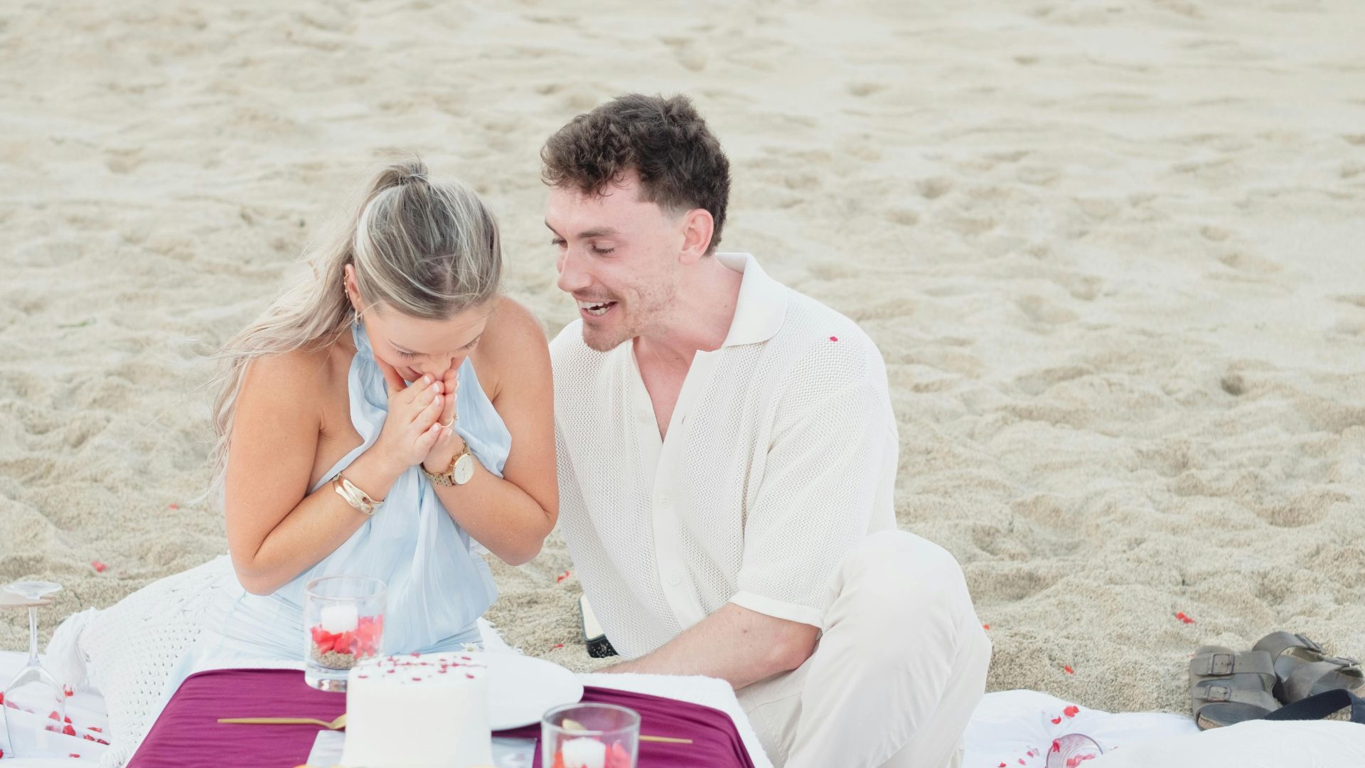 A couple enjoying a romantic picnic on the beach with a celebration cake and fruit.