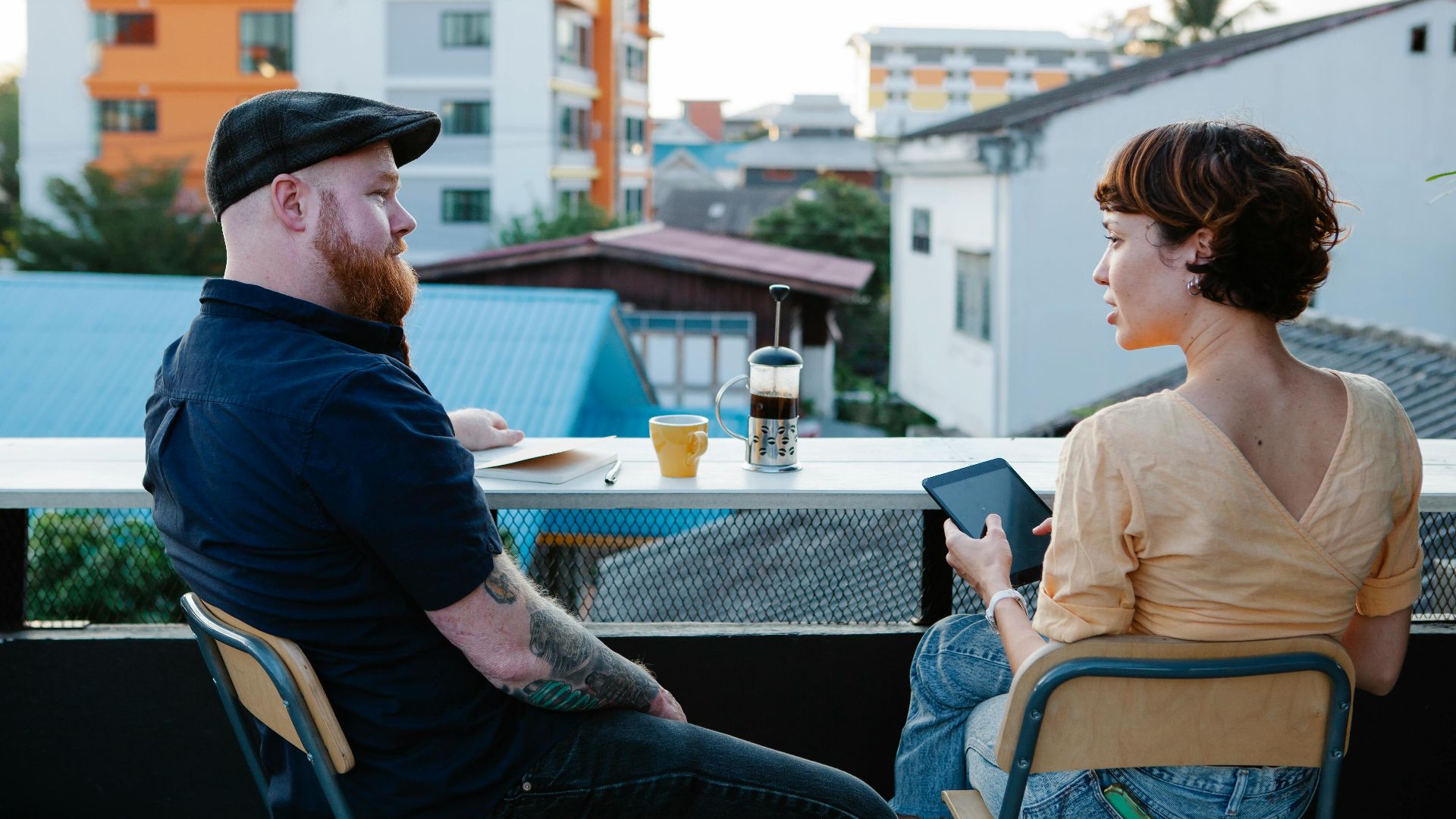 Back view of young woman with tablet and stylish man resting with cup of coffee in terrace in daytime