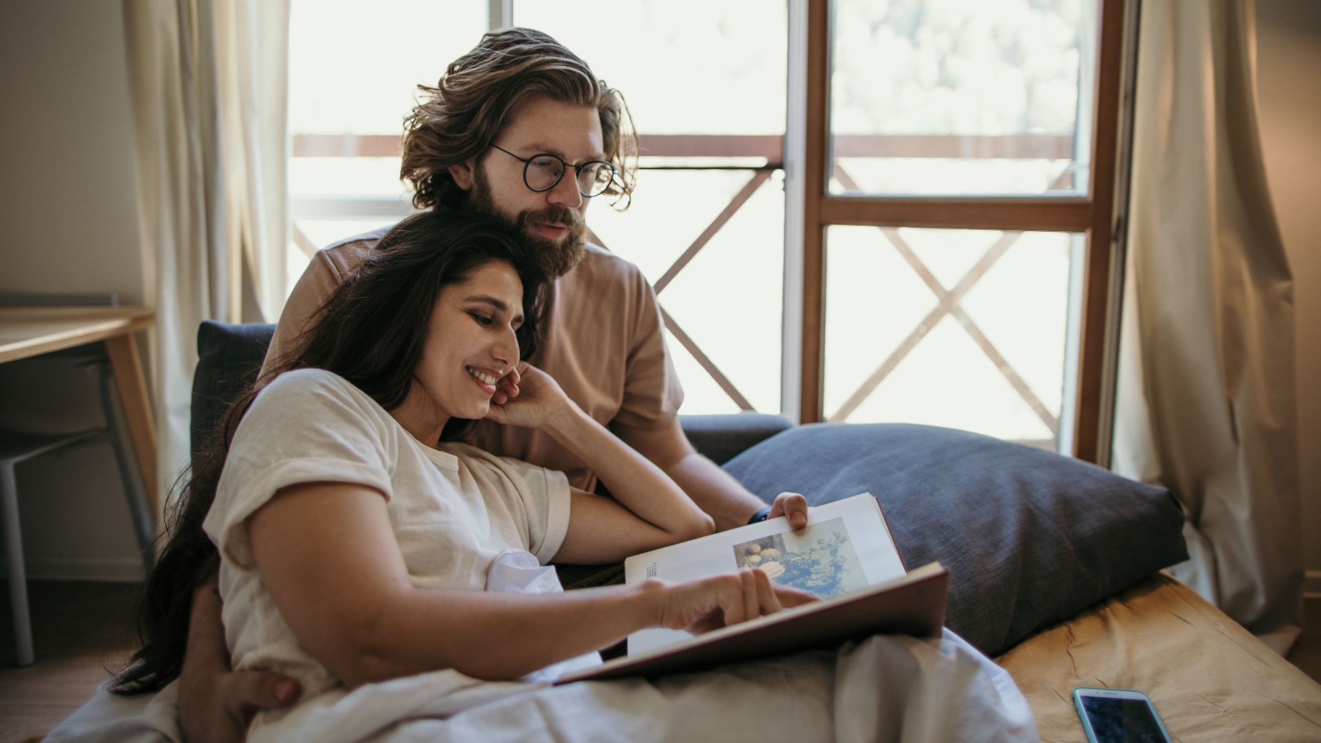 A couple enjoys a cozy morning reading together in their bedroom, embracing love and togetherness.