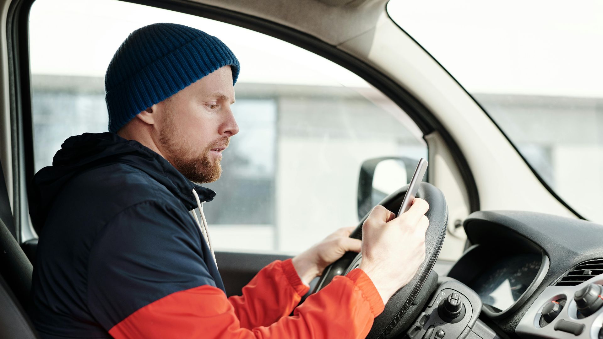 Distracted driver uses a smartphone in a car, highlighting road safety concerns.