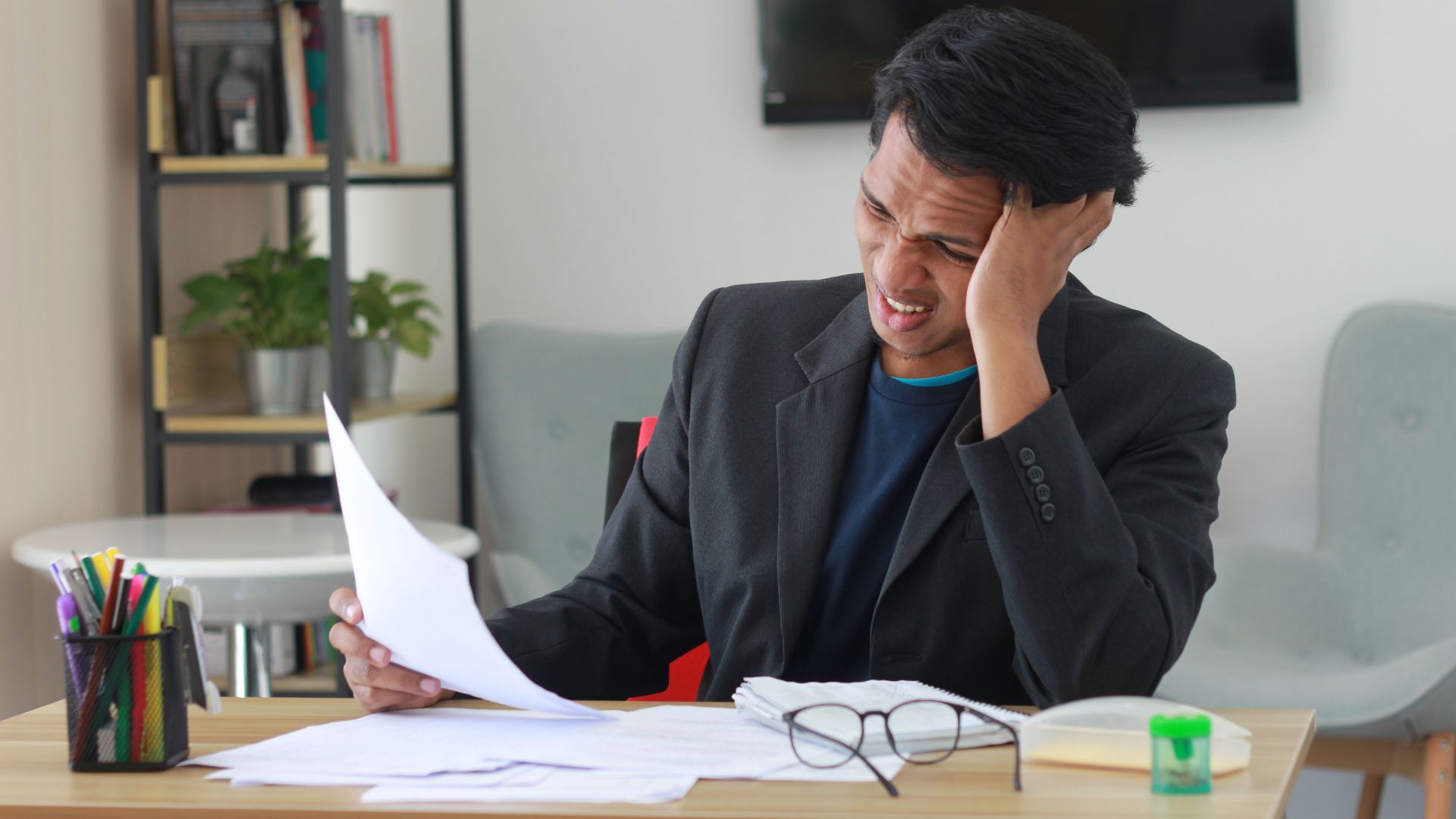A businessman in an office experiencing stress while reviewing documents.