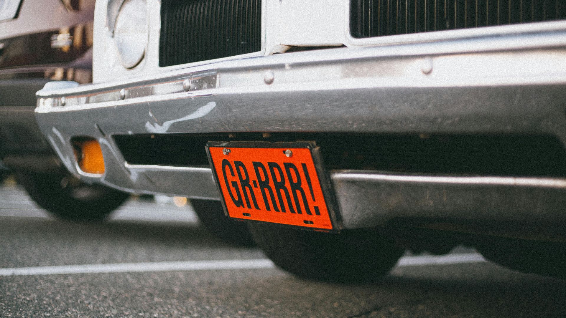 Close-up of a vintage car with a custom orange license plate reading 'GR-RRR!' in a parking lot.