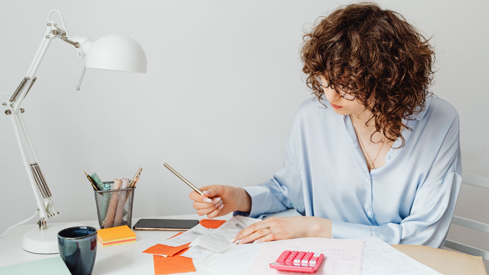 Woman in office calculating expenses with documents, calculator, and coffee.