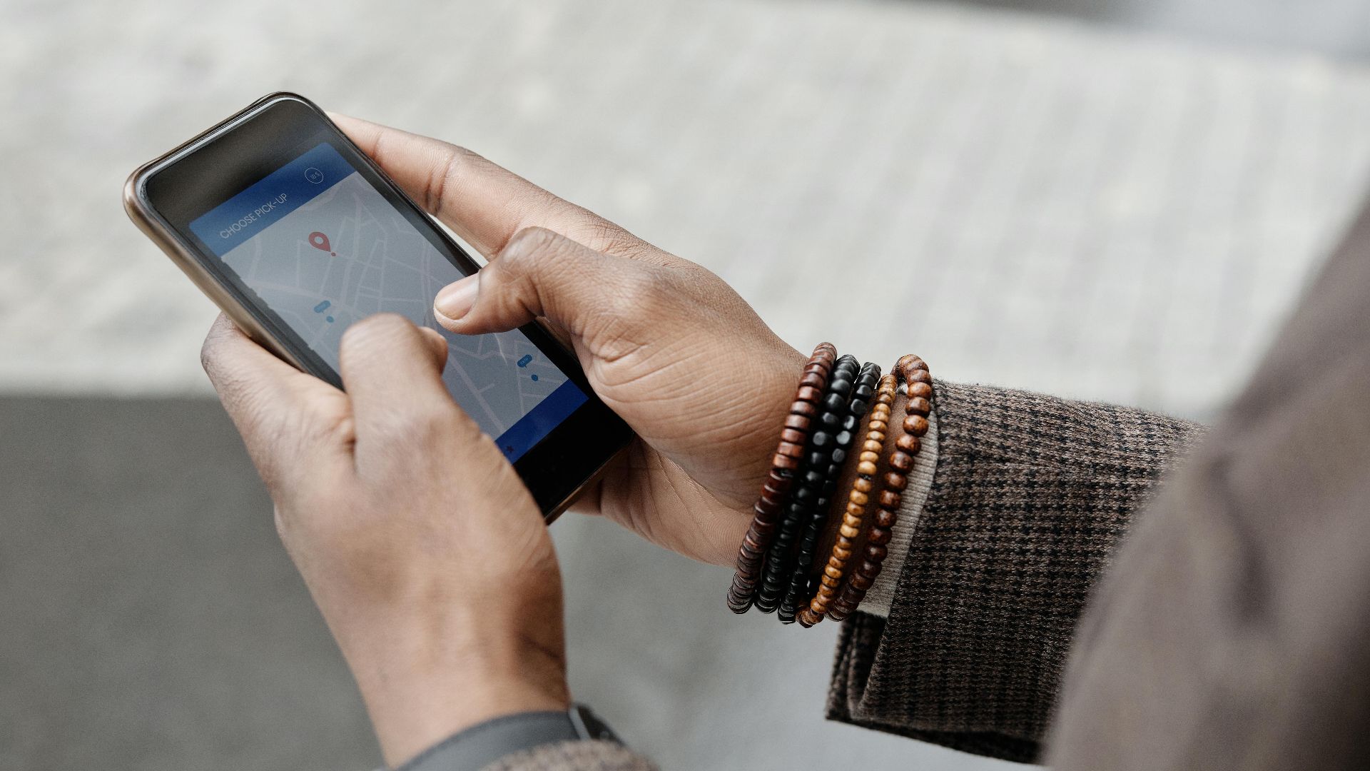 Close-up of hands with bracelets navigating on smartphone using GPS app outdoors.