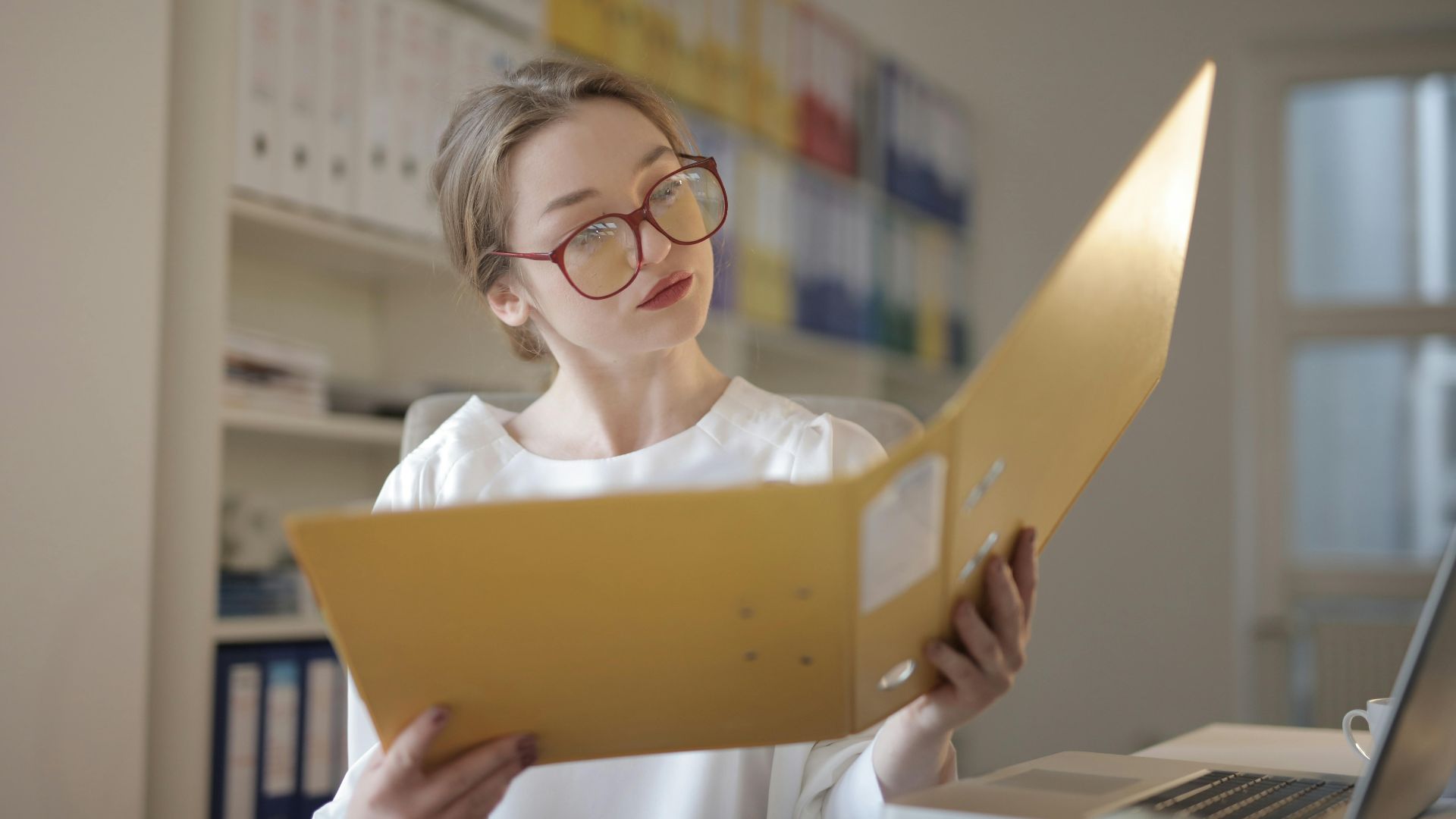 Caucasian woman intensely reading documents in an office setting.