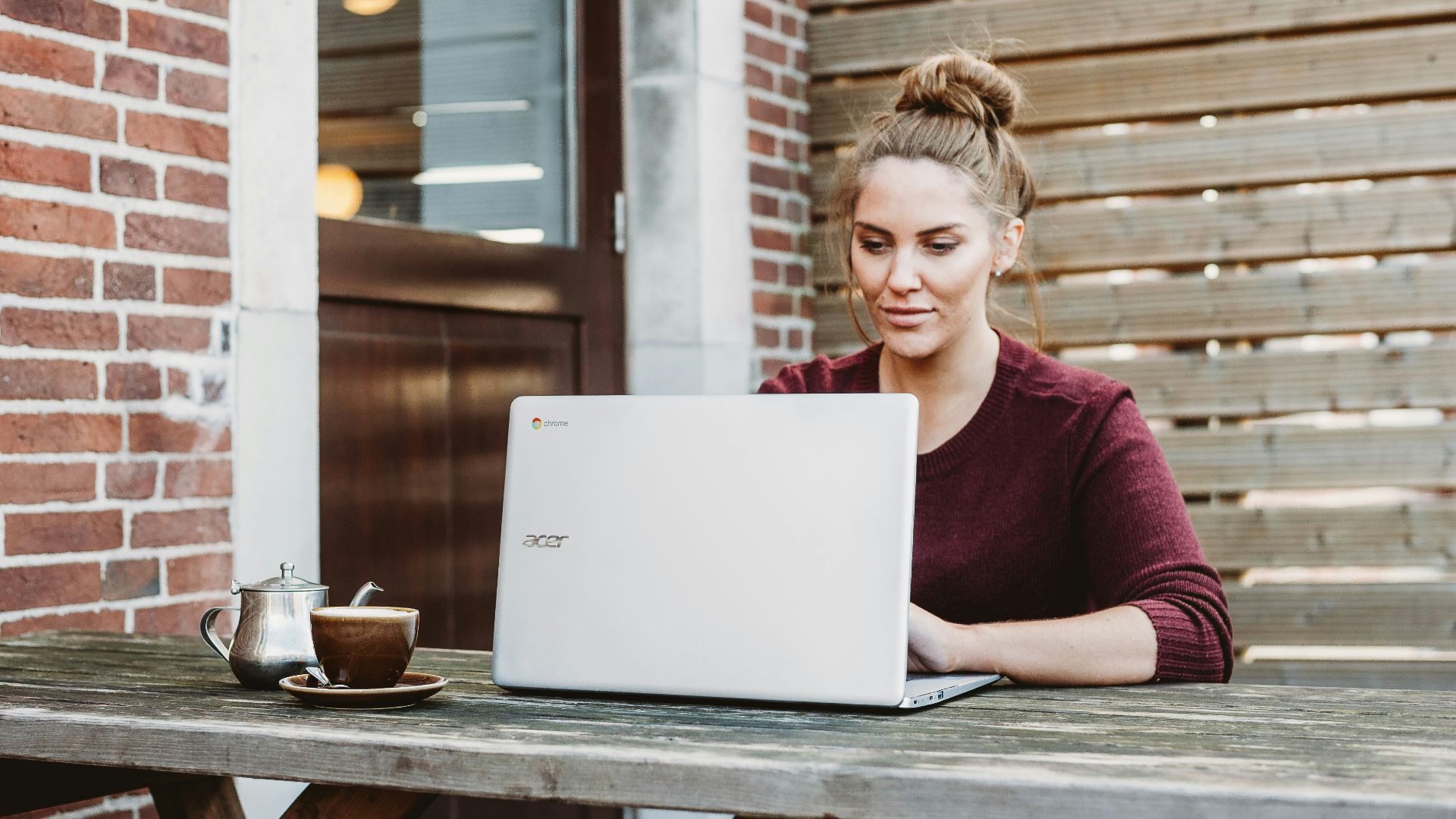 woman sitting and holding white Acer laptop near brown wooden wall