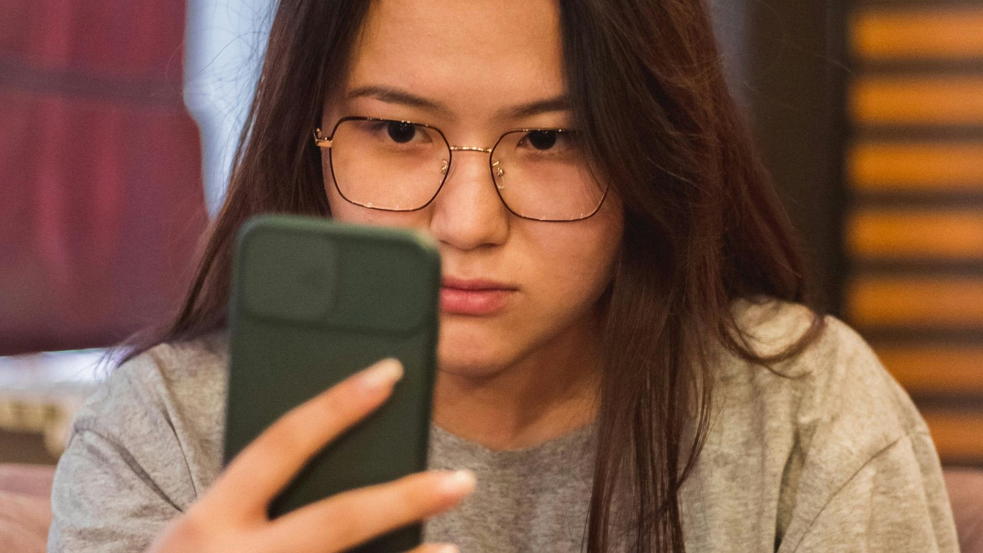 Focused young woman with glasses using her smartphone indoors.