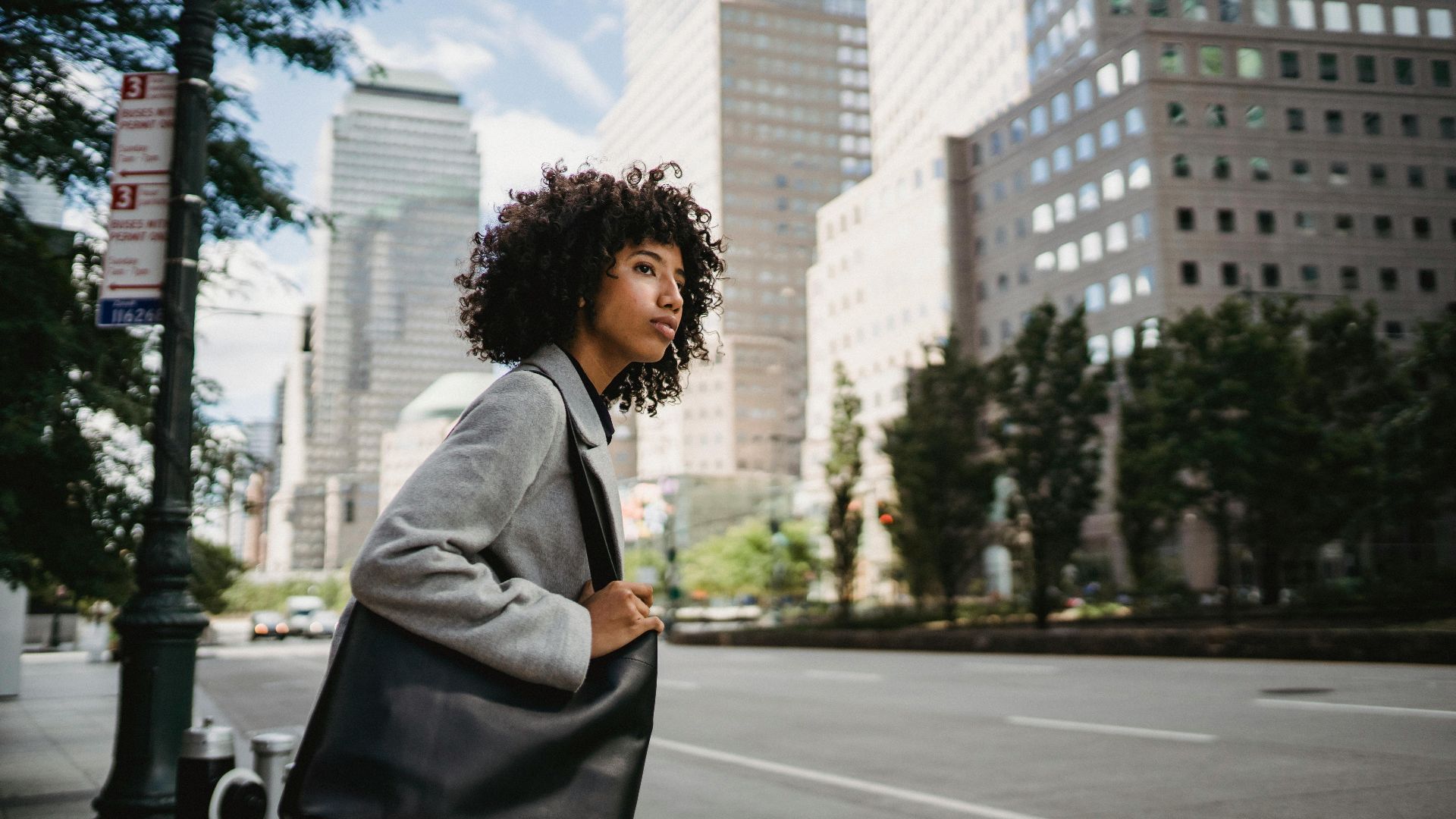 A fashionable woman with a leather bag crossing the street in a bustling city setting.