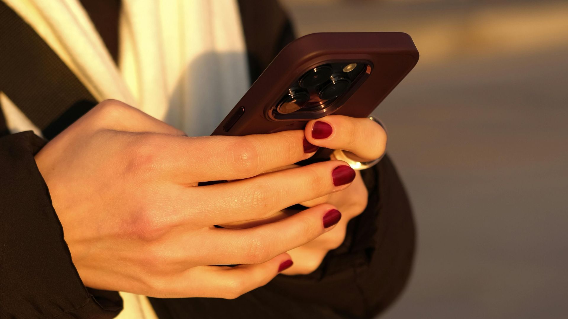A woman with red nails using a smartphone outdoors in İstanbul.