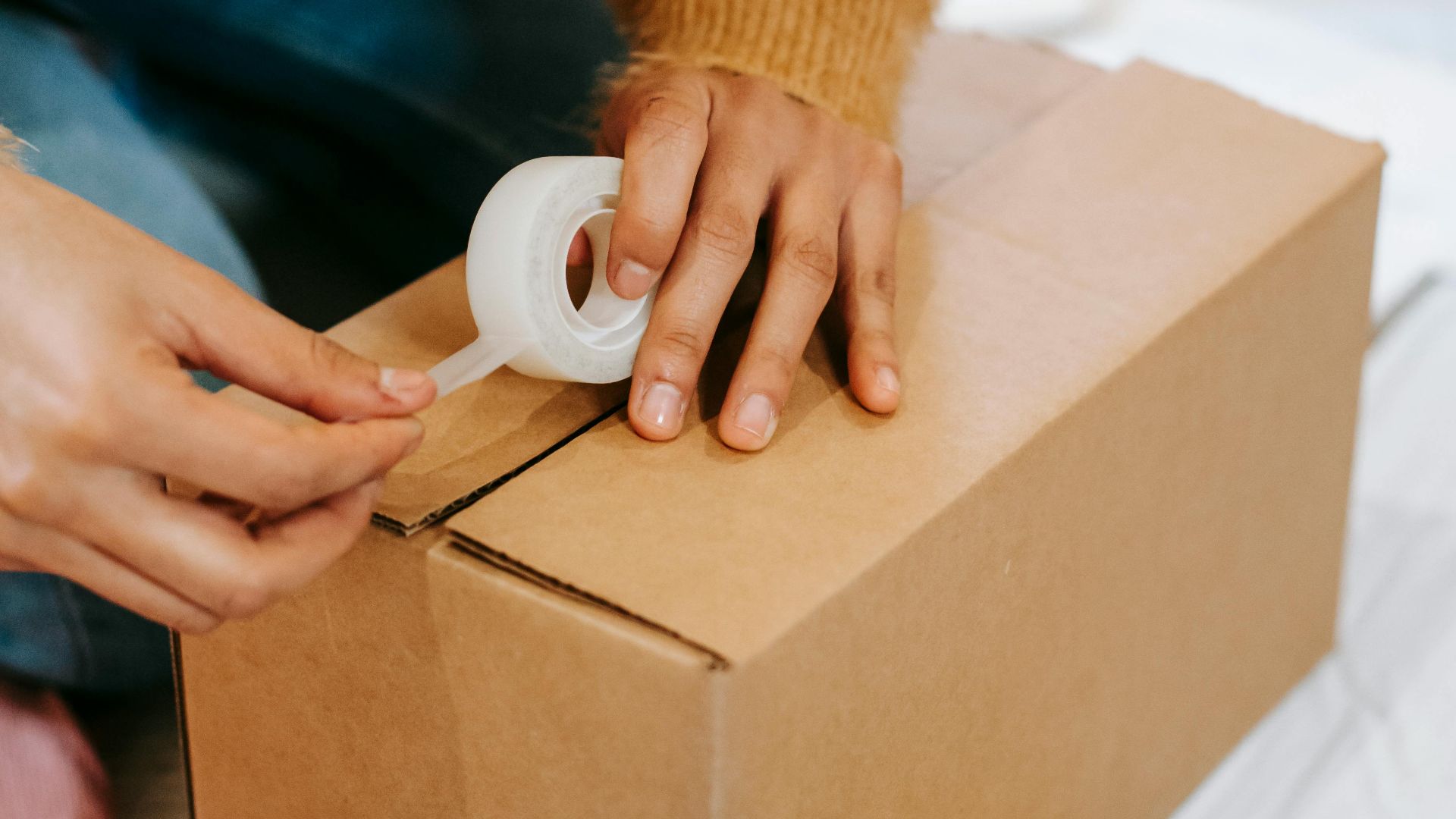 From above of crop anonymous female preparing parcel in carton box on floor among clothes