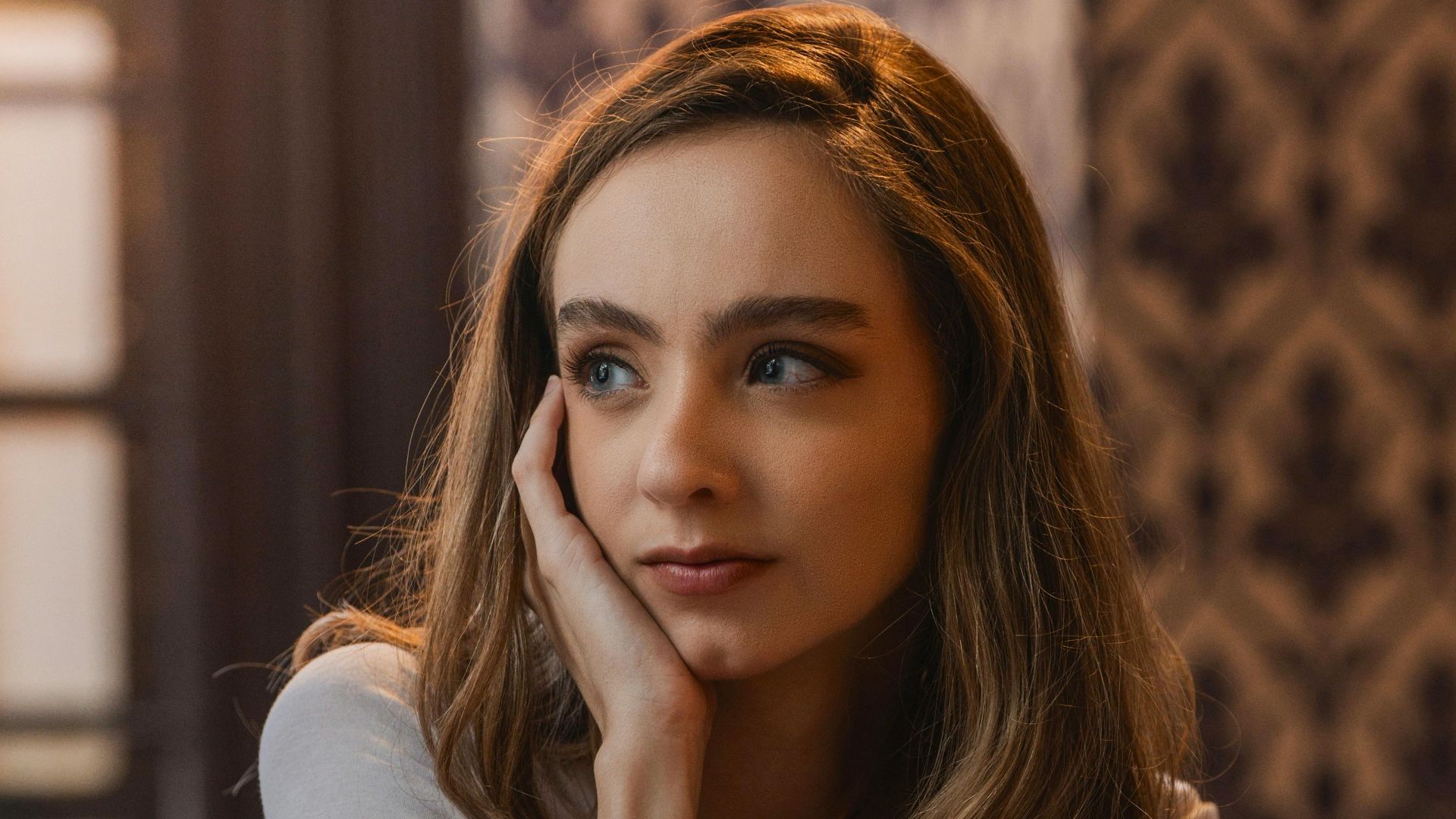 A contemplative young woman reads a book in a warmly lit, stylish cafe.