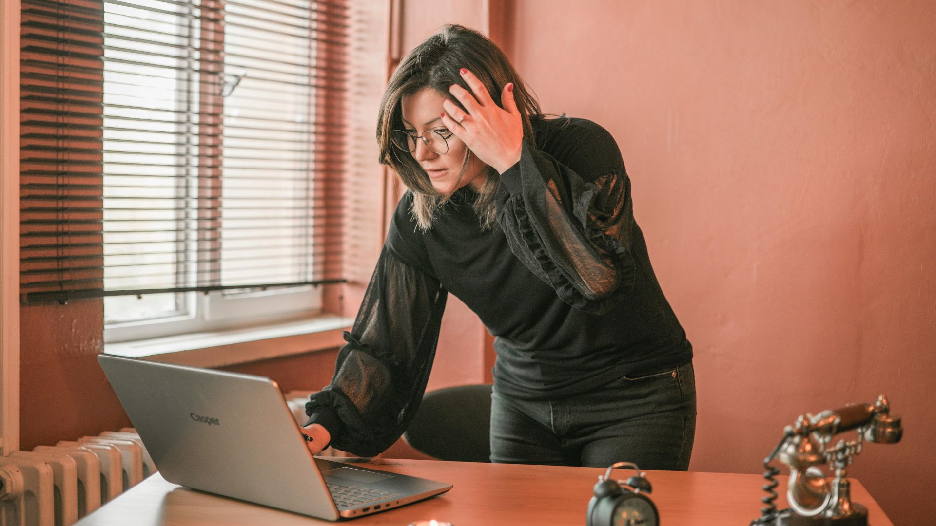Businesswoman stands focused on her laptop in a stylish office with warm lighting.