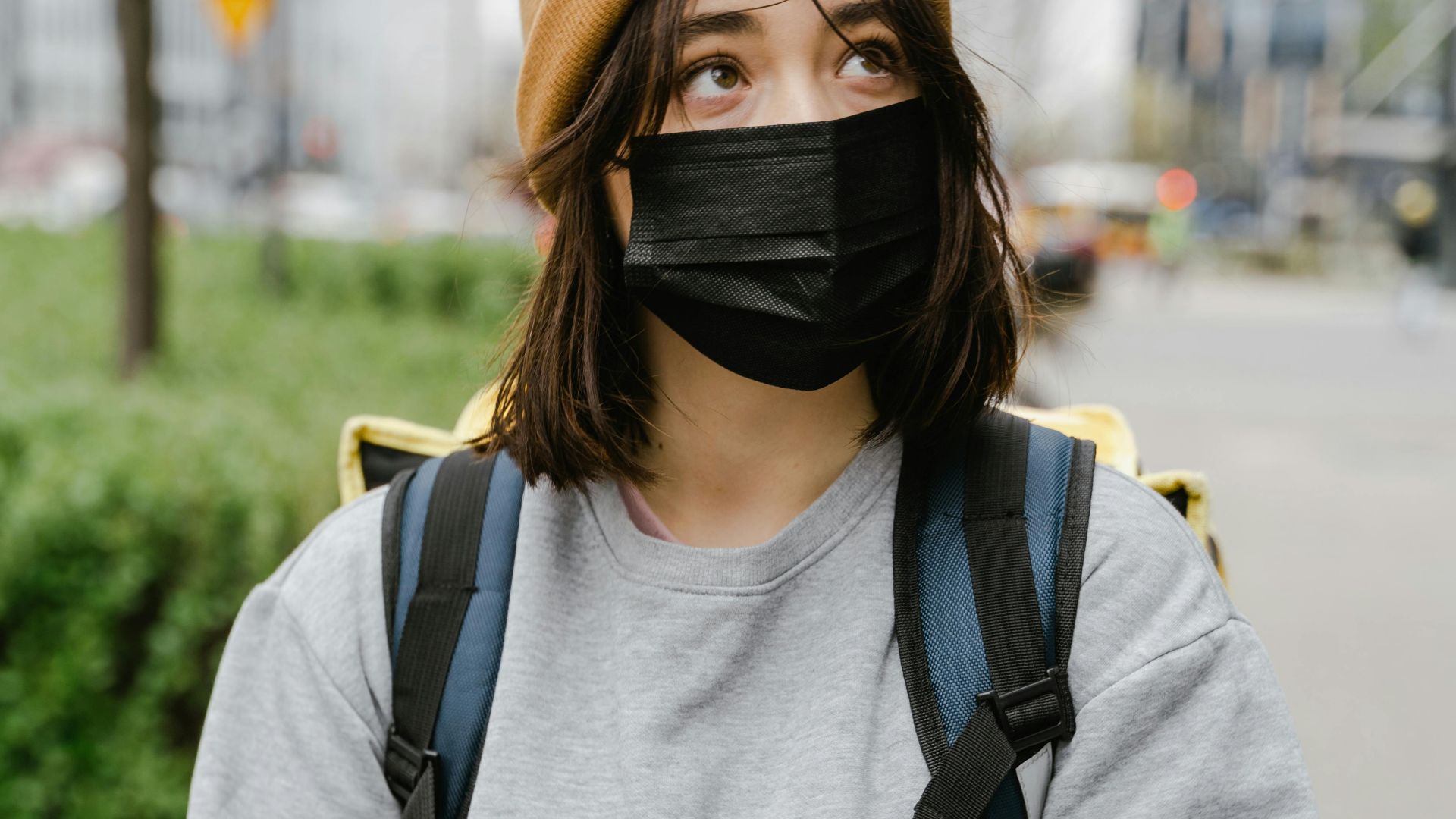 A woman wearing a face mask checks her phone while outdoors in the city.