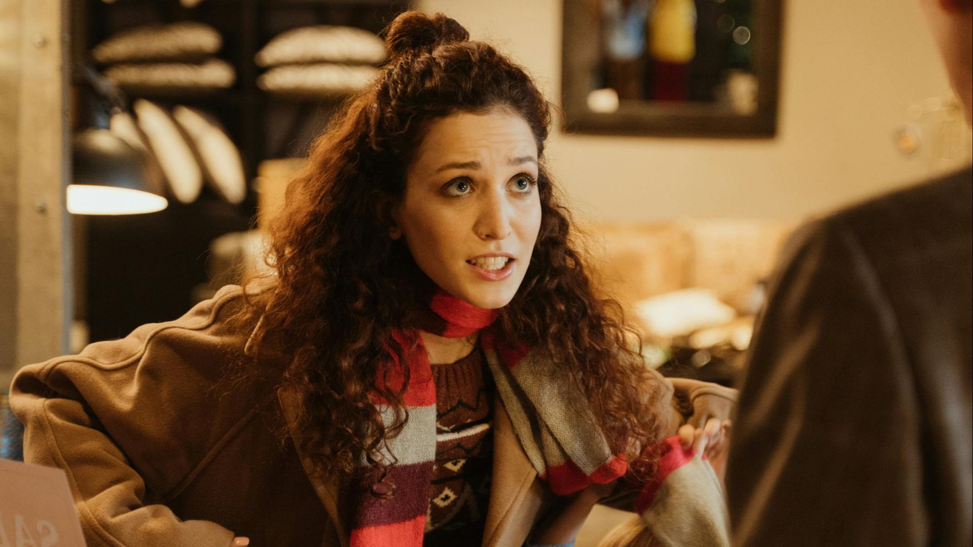 Woman at the counter in a cozy store, engaging with a shopkeeper, surrounded by holiday decor.