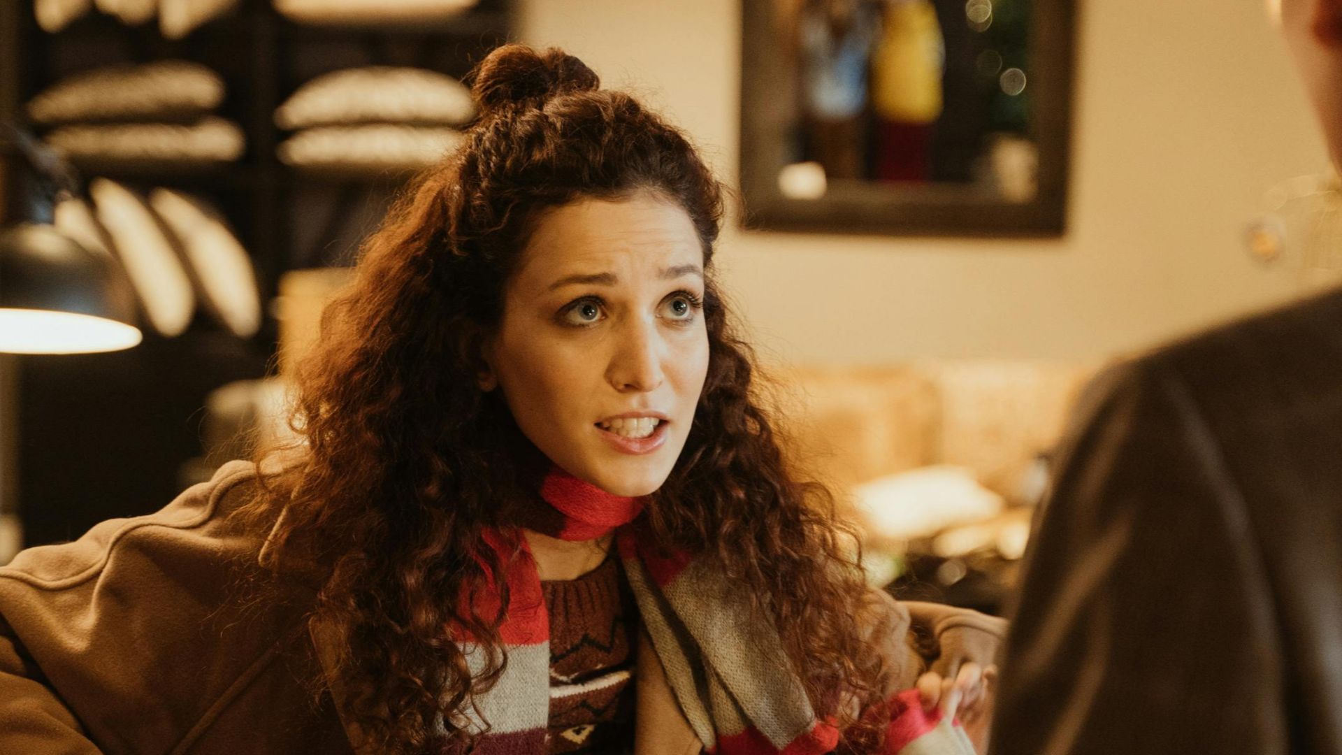 Woman at the counter in a cozy store, engaging with a shopkeeper, surrounded by holiday decor.